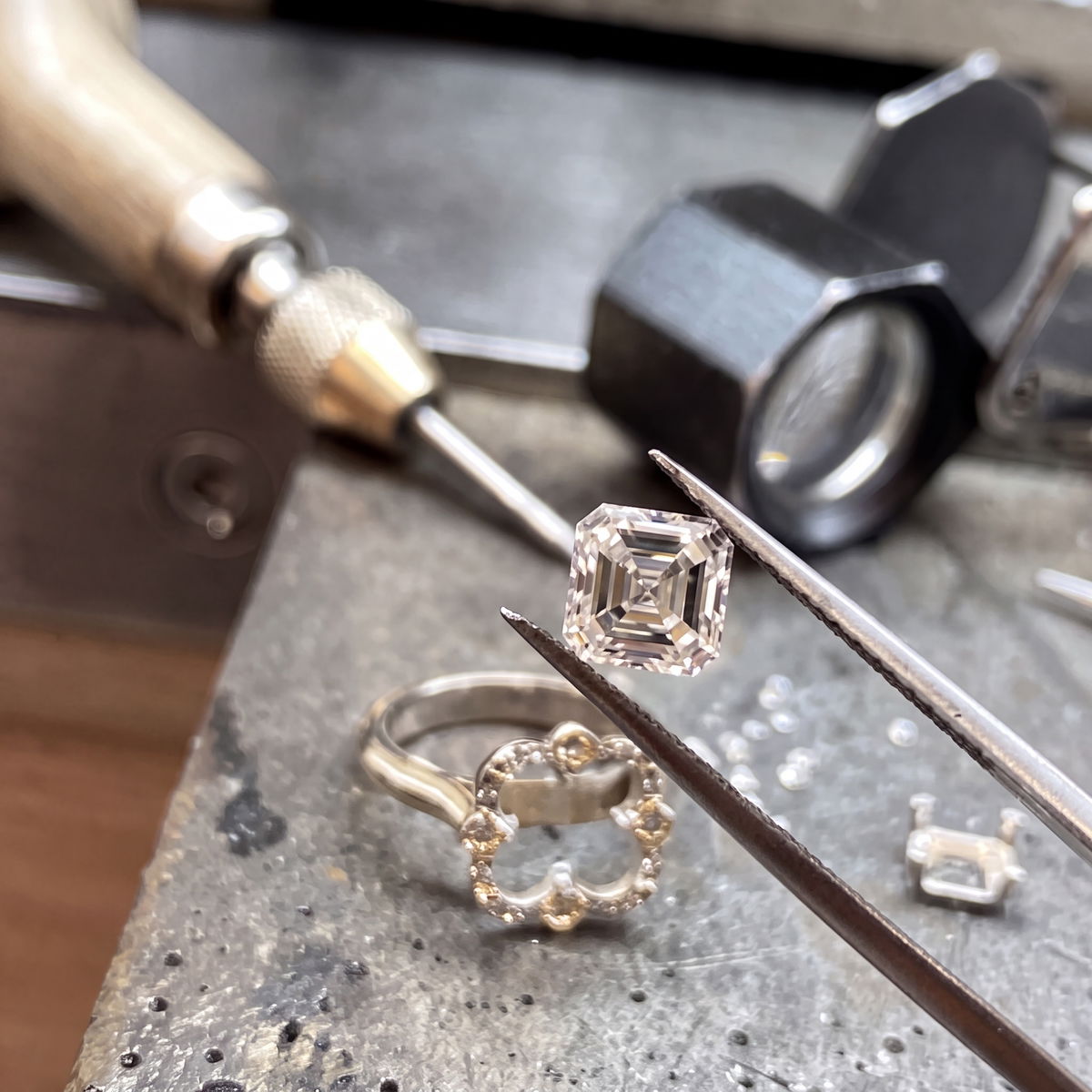 Jeweler repairing a diamond ring at the bench with precision tools, loupe and tweezers
