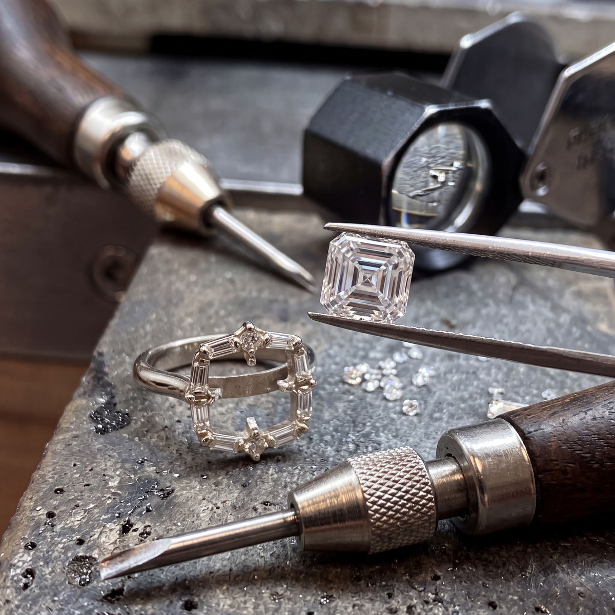 Jeweler using a hand tool and tweezers to repair a diamond ring at a workbench