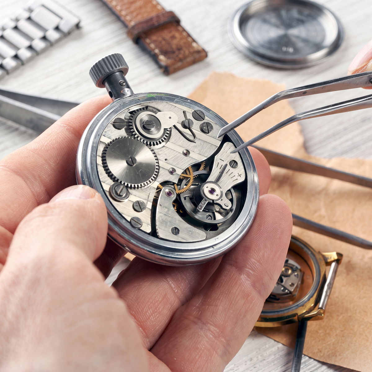 Watchmaker using tweezers to service the movement of a mechanical pocket watch