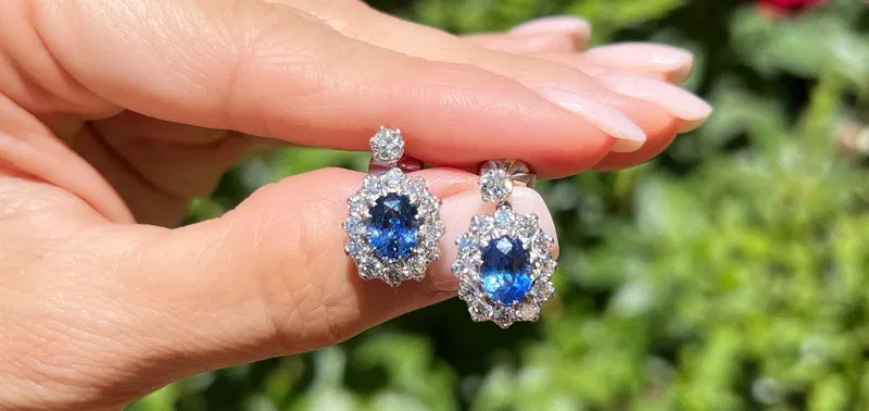 Sapphire and diamond cluster earrings held in hand