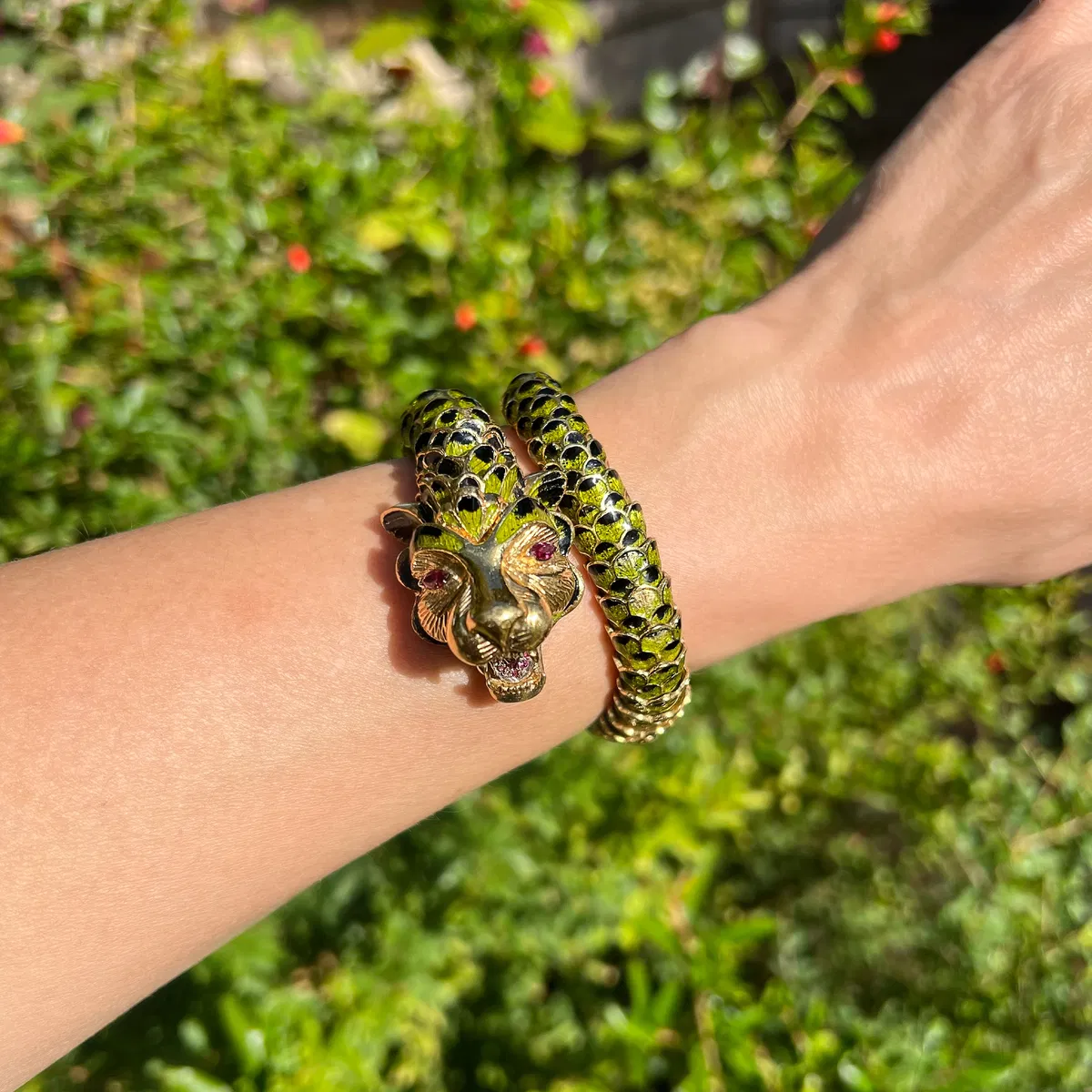 A gold and enamel panther wrap bangle on the wrist in a garden