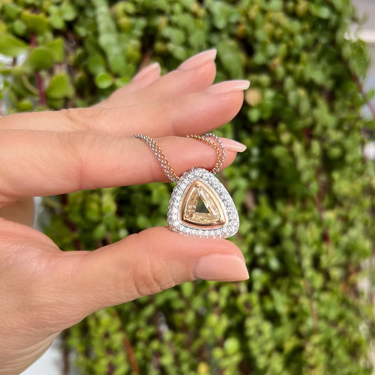 A trillion diamond pendant held in hand against a creeping-fig wall