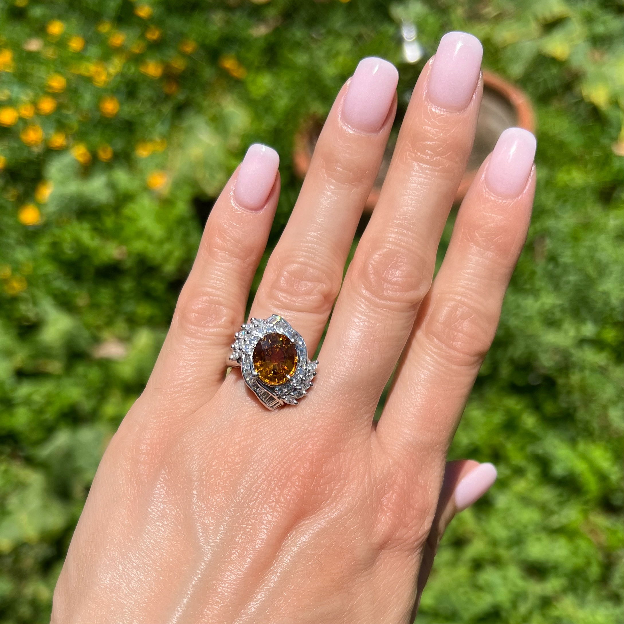 This stunning Platinum 6.46ct Oval Strong Orange Sapphire & 1.16tcw Diamond Ring 12.6g is the perfect choice for the discerning jewelry connoisseur. This show-stopping ring is crafted from solid Platinum and is adorned with a 6.46ct Oval Strong Orange Sapphire gemstone, featuring a 1.16tcw of brilliant Diamonds accenting it to perfection. The shanks of this piece are stamped with Pt850 D1.16 S6.89 and the center known weight is 6.46ct. This beautiful ring comes with a Carte Blu Certification verifying the Sapphire is Natural Sapphire with only standard hear enhancement. Get this stunning Estate Platinum Diamond Sapphire Ring today! Platinum 6.46ct Oval Strong Orange Sapphire & 1.16tcw Diamond Ring 12.6g, s6.75