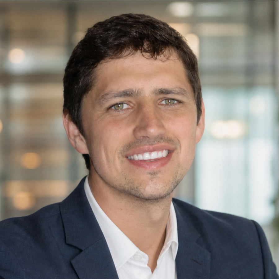 Flawless POS Team Member Headshot – Gert Nortje Smiling man with short dark hair and stubble seated in an office chair, framed photos on wall behind him