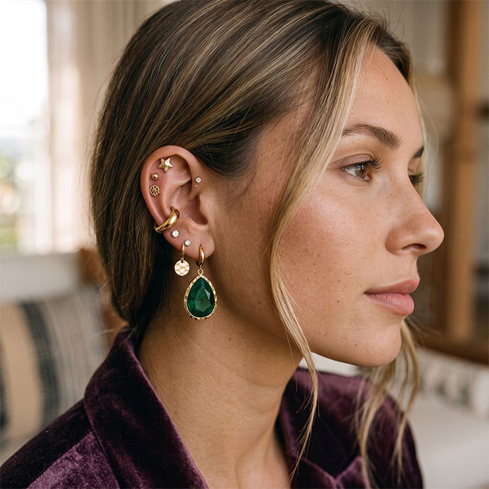Bold gold earring stack with hoop, gemstone drop earring, and accent studs for special occasion.