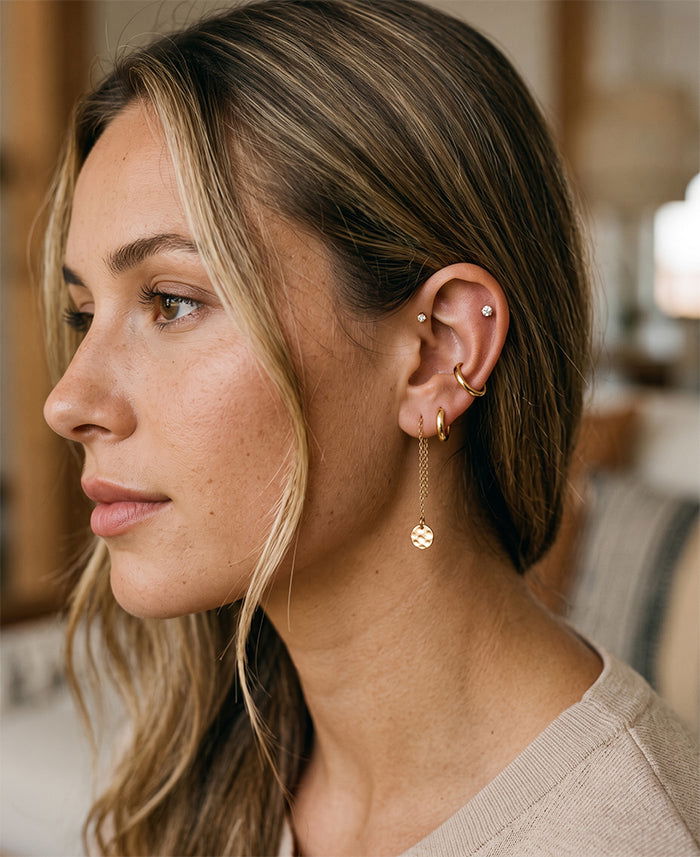Gold earring stack with stud, huggie hoop, and dangle earring on multiple ear piercings.