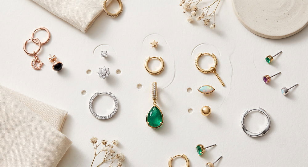 Assorted gold earring stack pieces including gemstone drop, studs, and hoop laid flat.
