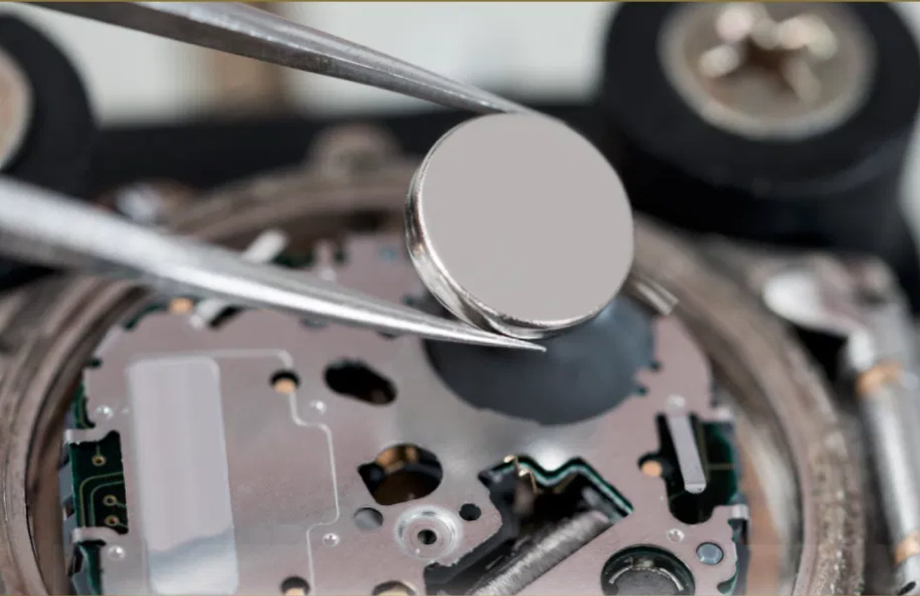 Watchmaker using tweezers to place a new battery cell into an open watch movement