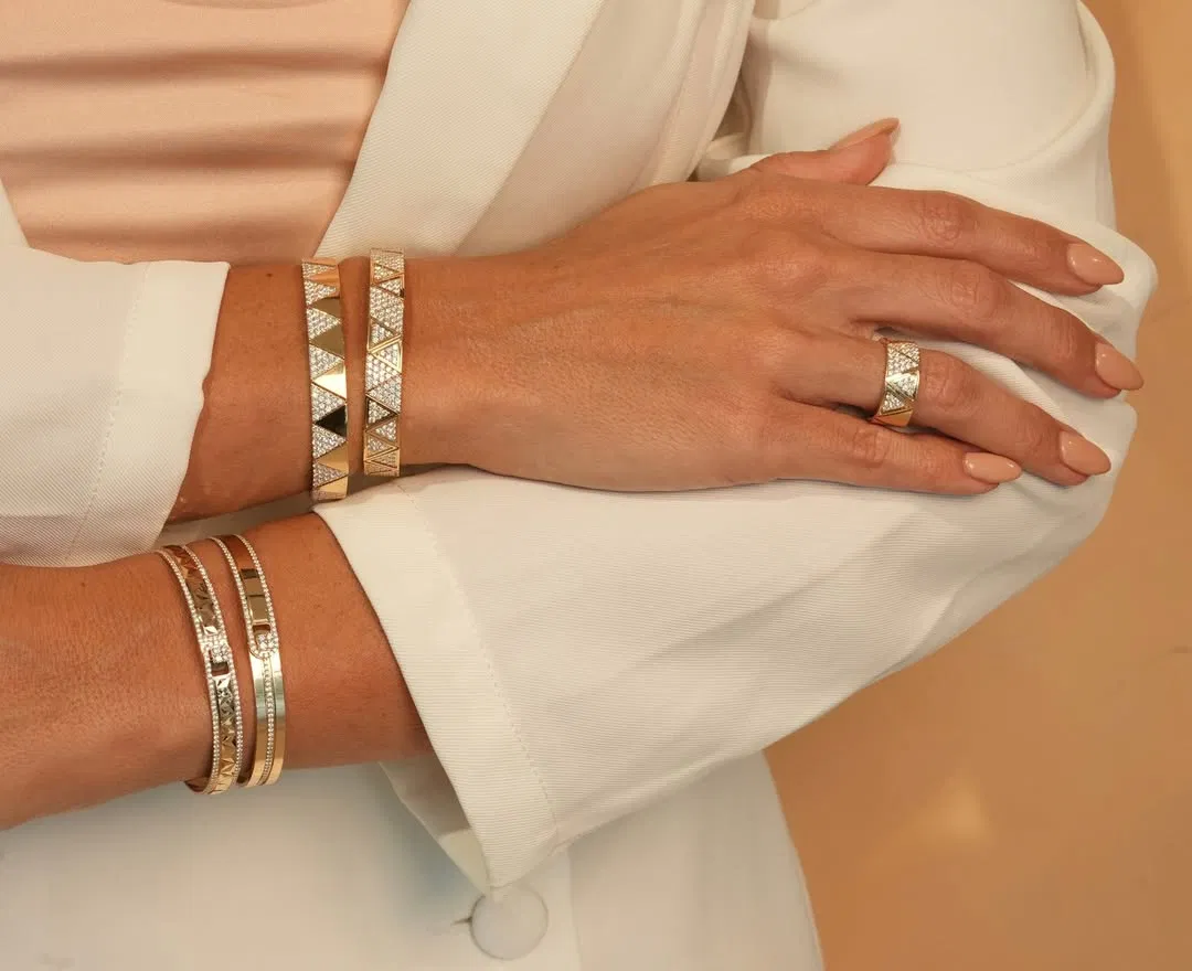 Stacked gold bangles and rings on a white sleeve