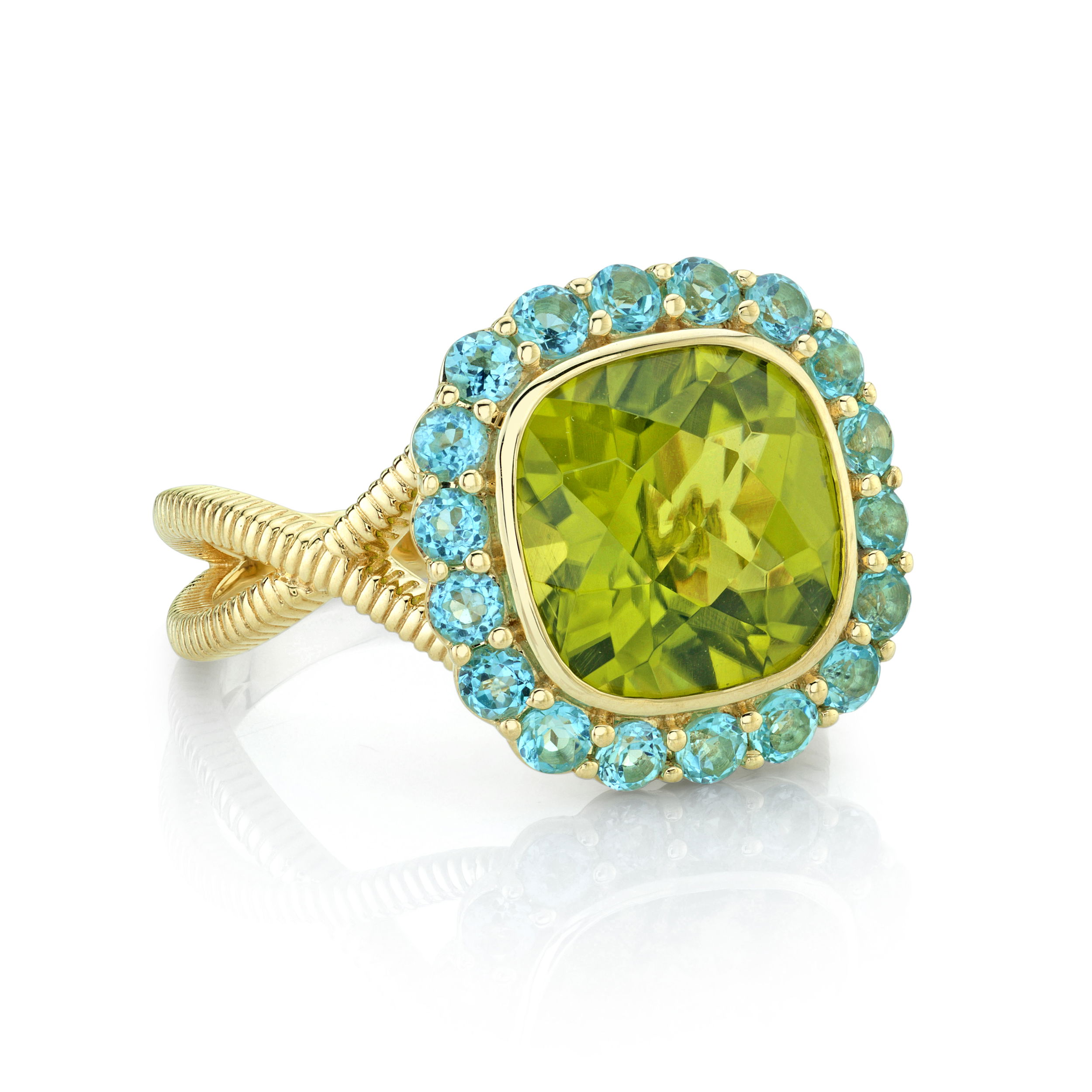 Peridot Center Stone Ring with Swiss Blue Topaz Halo in 18kt Yellow Gold by Sloane Street Jewelry. Cushion cut Peridot ring with Swiss Blue Topaz halo and strie texture split shank in 18kt yellow gold - 4.34ct enhanced Peridot at the center and enhanced color Swiss blue Topaz at 0.92ctw Peridot Center Stone Ring with Swiss Blue Topaz Halo in 18kt Yellow Gold