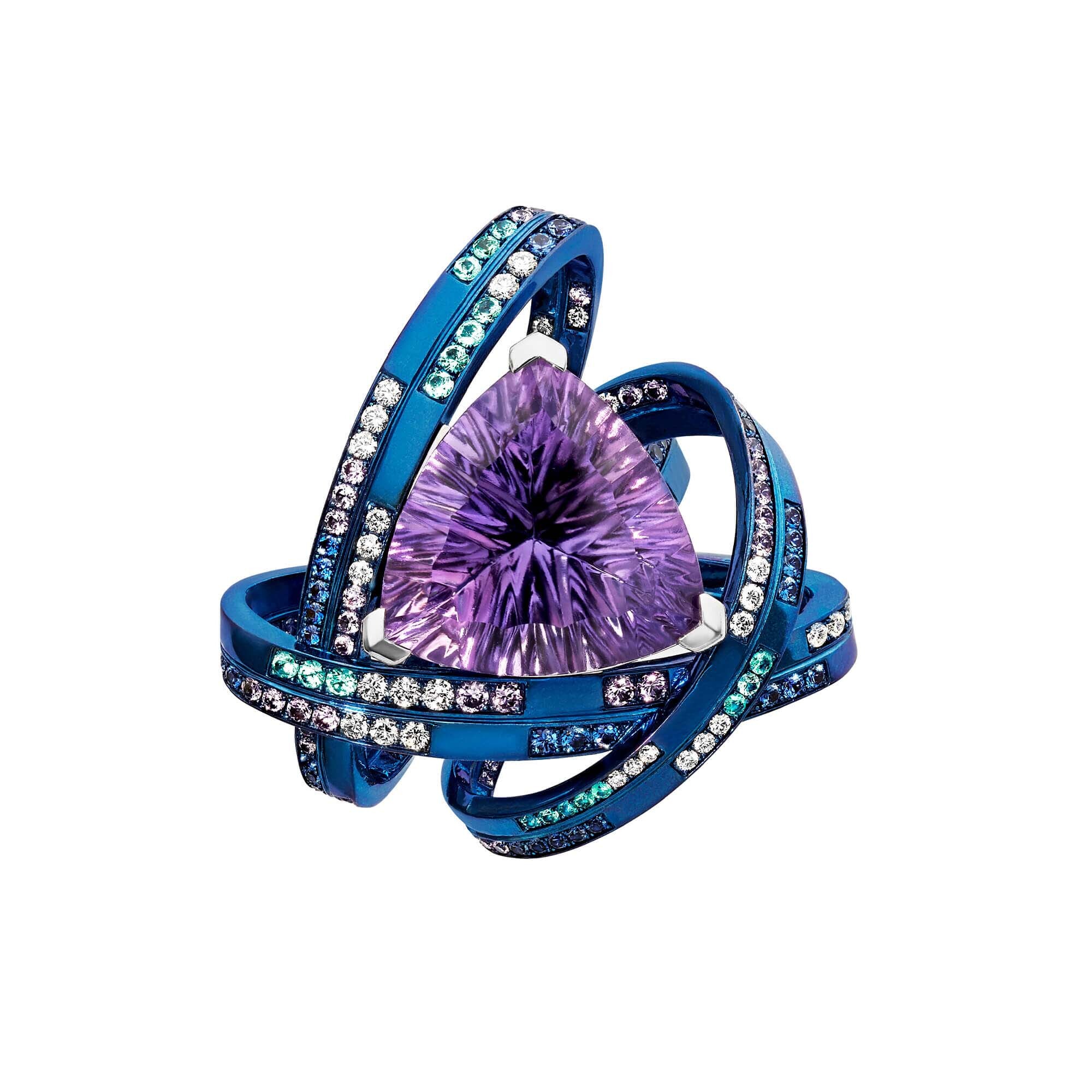 The Rebelles Rocket Girl Ring with Amethyst in 18kt White Gold, Palladium and Titanium - Size 7 by Stephen Webster. The ReBelles - Rocket Girl - 18kt White Gold, Palladium and Titanium ring set with a center Amethyst in Trillion dynamite cut with white diamonds, blue sapphires, pink sapphires and Paraiba tourmalines. Ring number 6 of 10. Visualizing the mathematical genius, Katherine Johnson, who was the original human calculator and played a pivotal role in space exploration. Set in Blue Titanium on a White Gold shank, with a central Trillion Dynamite Cut Amethyst (shown in 18.30ct) with Paraiba Tourmalines, Diamonds, Purple and Blue Sapphires. Limited production of 10 per design. Each piece is numbered and engraved with ROCKET GIRL. The Rebelles Rocket Girl Ring with Amethyst in 18kt White Gold, Palladium and Titanium - Size 7