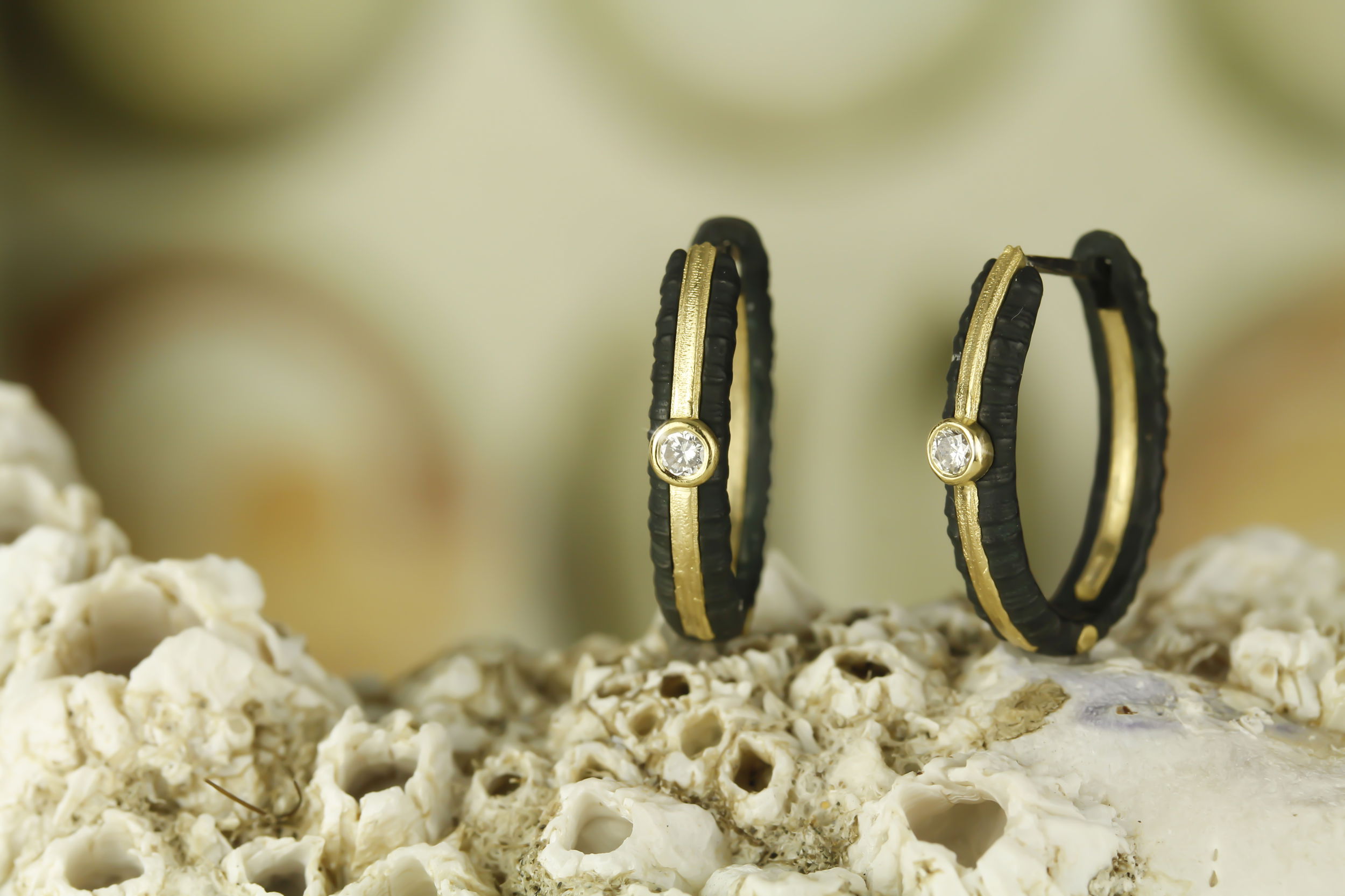 Ridge Hinged 18mm Oval Hoop Earrings with White Diamonds in 18kt Yellow Gold and Black Chrome by Sarah Graham Metalsmithing. The Ridge Hinged Oval Hoop measures 18mm long and has a gold inside-out stripe. The earrings are set with 0.10ctw of white diamonds shining brightly against the velvety black. The stripe and accents are created in 18kt yellow gold. Ridge Hinged 18mm Oval Hoop Earrings with White Diamonds in 18kt Yellow Gold and Black Chrome