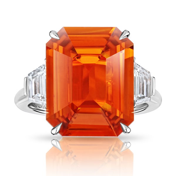 Closeup photo of 10.53ct Emerald Cut Orange Sapphire with two trapezoid step cut diamonds at 1.02ctw set in a handmade platinum ring.