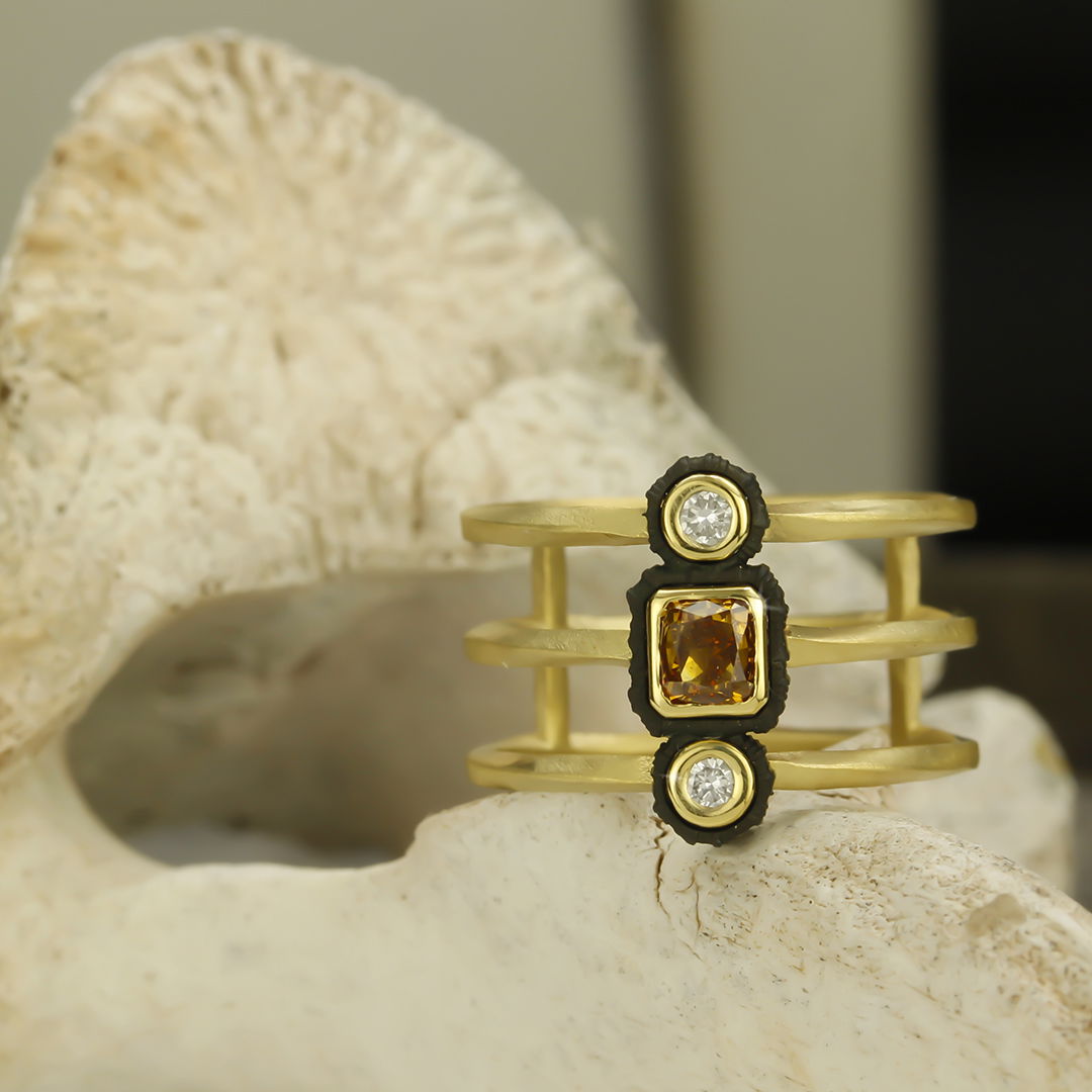 Twisted Triple Band Ring with White and Cognac Diamonds in Black Chrome and 18kt Yellow Gold by Sarah Graham. Stacked band on three levels in 18kt yellow gold and set with two white diamonds at 0.10ctw and one cognac diamond at 0.45ct surrounded by oxidized cobalt chrome. Twisted Triple Band Ring with White and Cognac Diamonds in Black Chrome and 18kt Yellow Gold