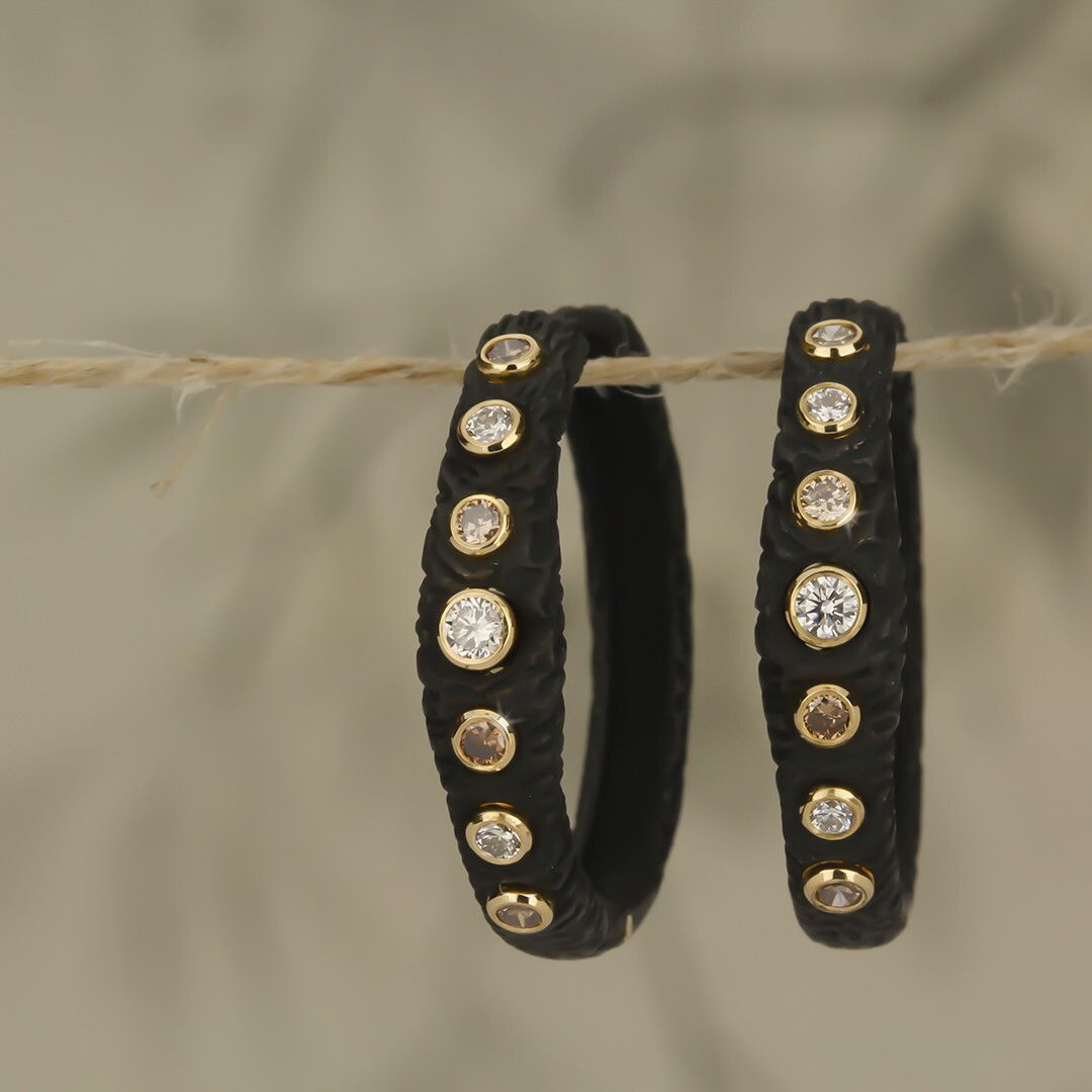 Pebble Bold Hinged 25mm Hoop Earrings with White and Cognac Diamonds in Black Chrome by Sarah Graham Metalsmithing. Each hinged Pebble hoop is created in black cobalt chrome and measures 25mm in diameter. The hoops are set with 0.46ctw of alternating white and cognac diamonds that shine bright against the black.? Each diamond is set in an 18kt yellow gold bezel. Pebble Bold Hinged 25mm Hoop Earrings with White and Cognac Diamonds in Black Chrome