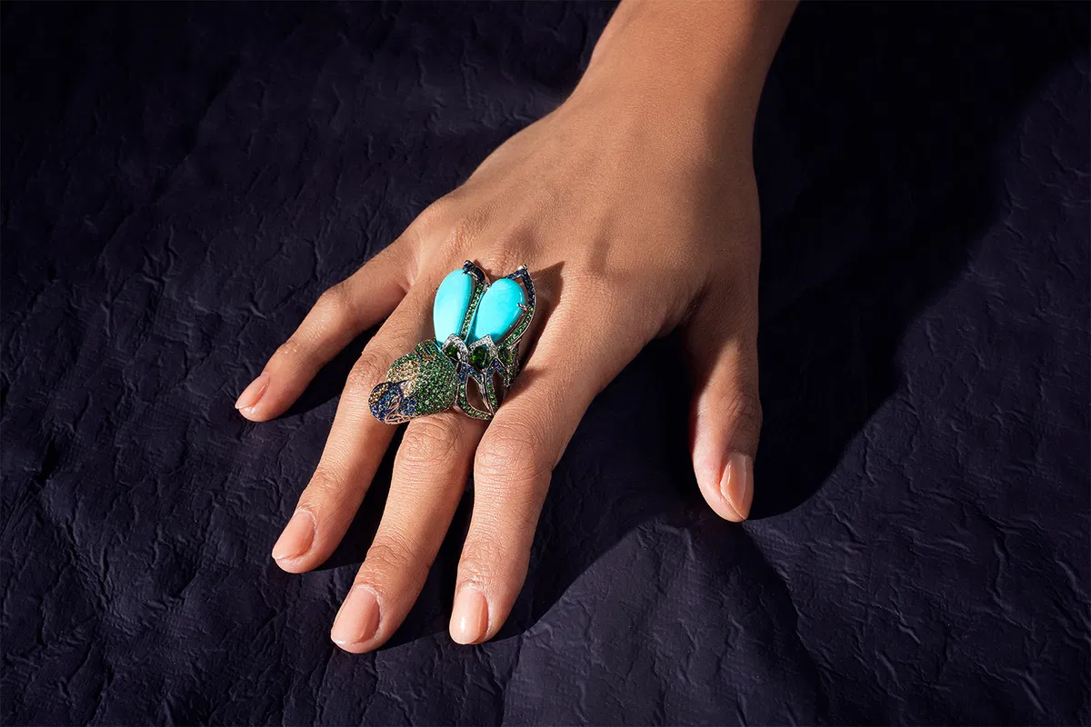 A hand wearing a turquoise and green peacock cocktail ring