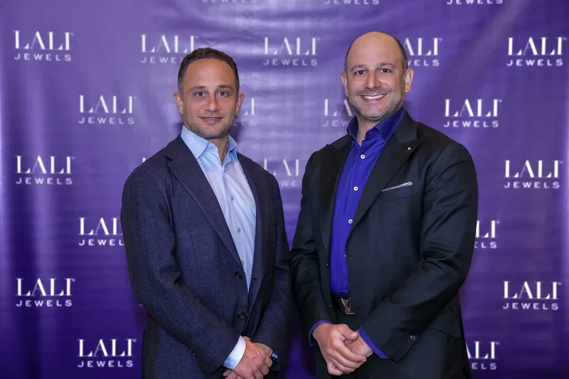 Two men in suits in front of a LALI Jewels backdrop