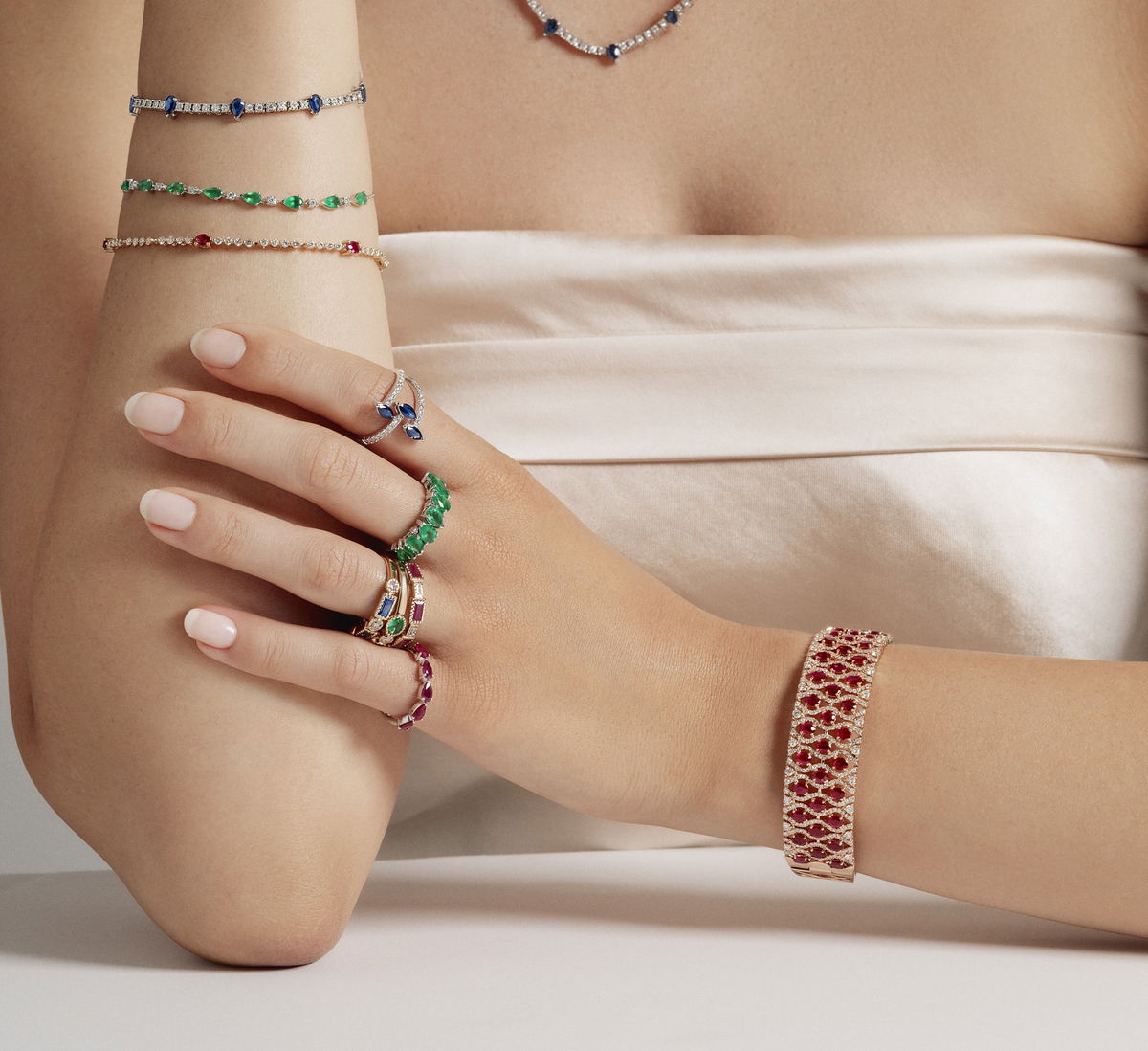A forearm with sapphire, emerald and ruby line bracelets