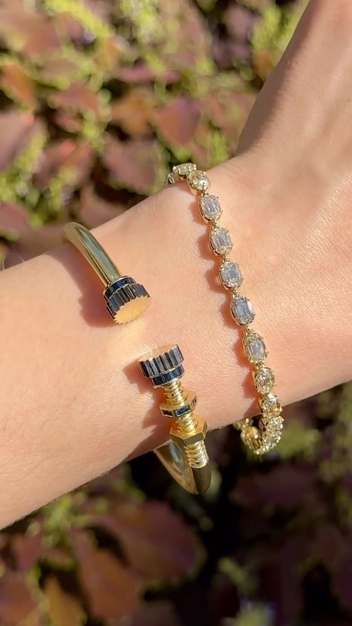 A gold cuff with blue stone ends and a diamond bracelet on the wrist