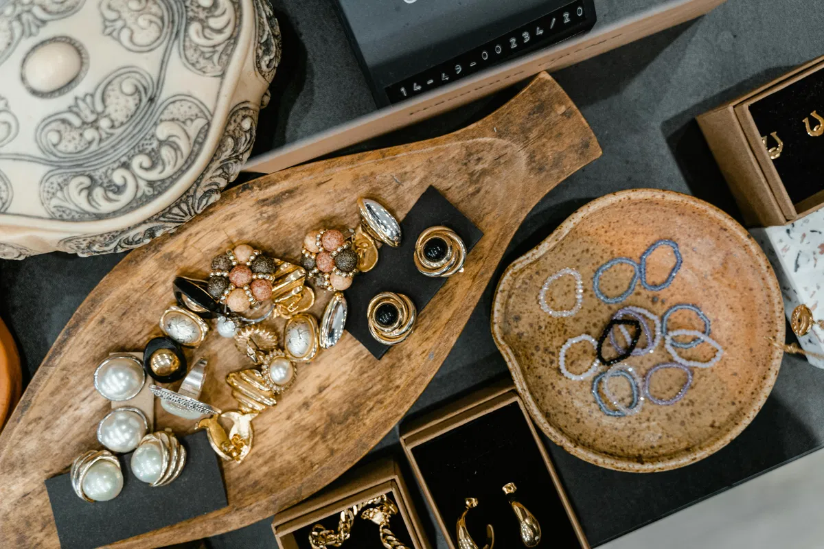 Assorted vintage jewelry and pearl earrings arranged on a wooden tray beside a ceramic dish