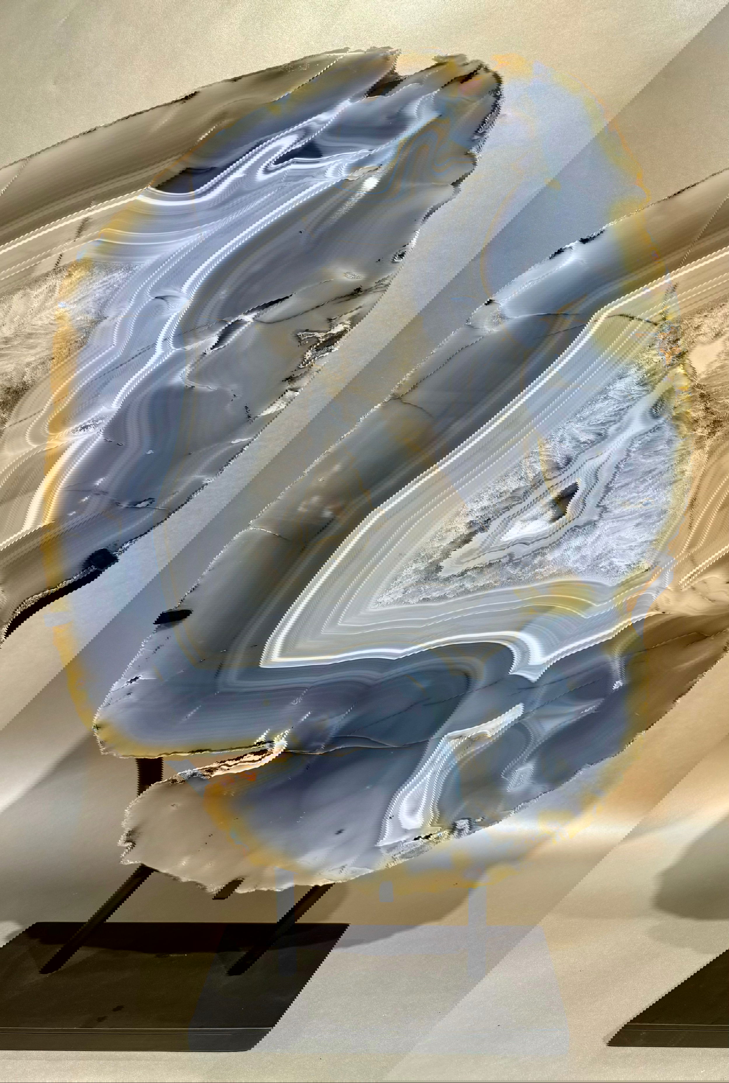 Elevate any space with the Freeform Thick Agate Slab. A blue agate rests upon a sleek metal base, creating a striking and elegant statement piece. Each slab is unique, adding an exclusive touch to your decor. Channel luxury and sophistication with this one-of-a-kind agate slab.Approx. 24.5" x 16". Freeform Thick Agate Slab