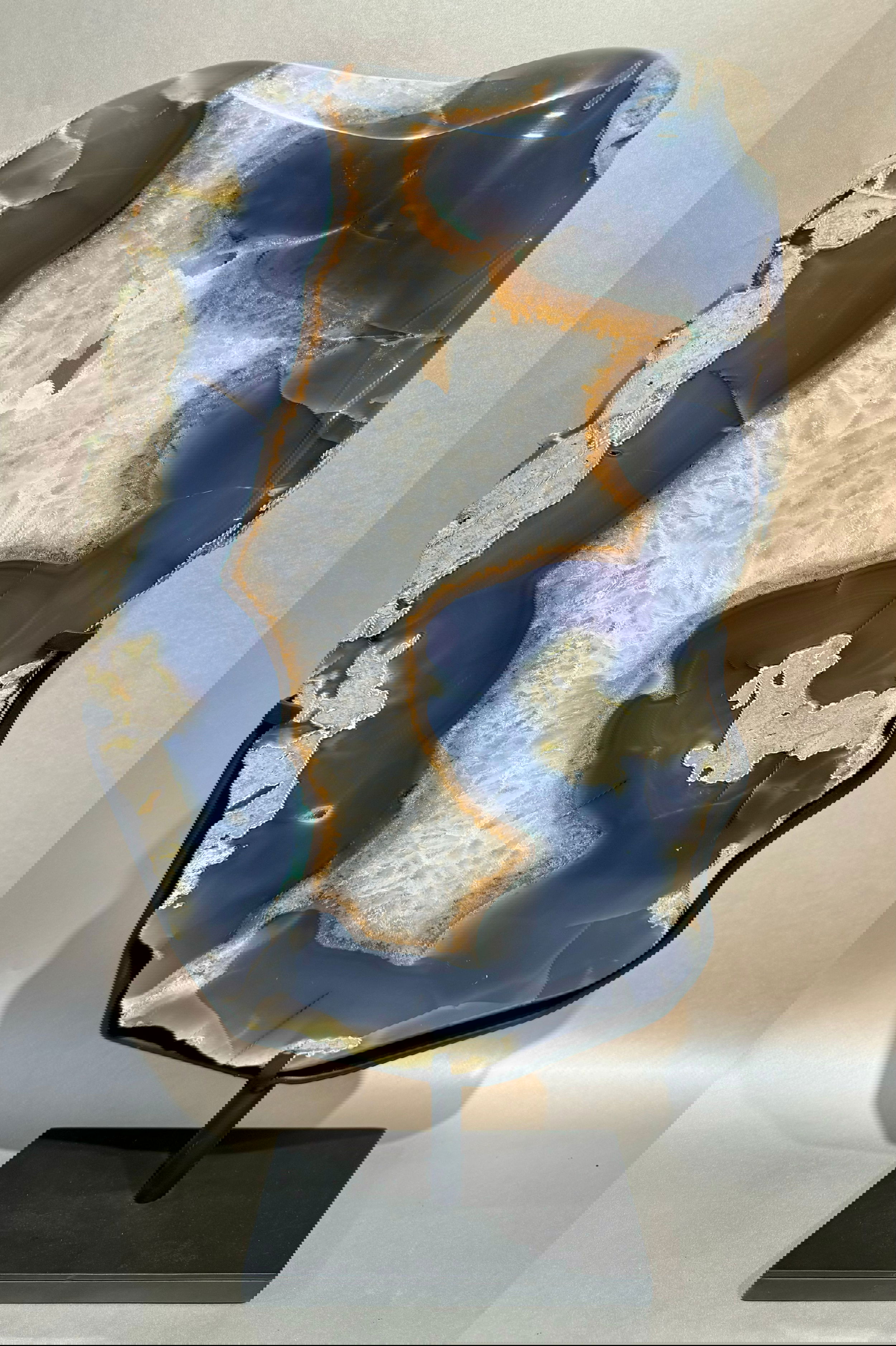 Elevate any space with the Freeform Thick Agate Slab. A blue agate rests upon a sleek metal base, creating a striking and elegant statement piece. Each slab is unique, adding an exclusive touch to your decor. Channel luxury and sophistication with this one-of-a-kind agate slab.Approx. 21" x 12". Freeform Thick Agate Slab