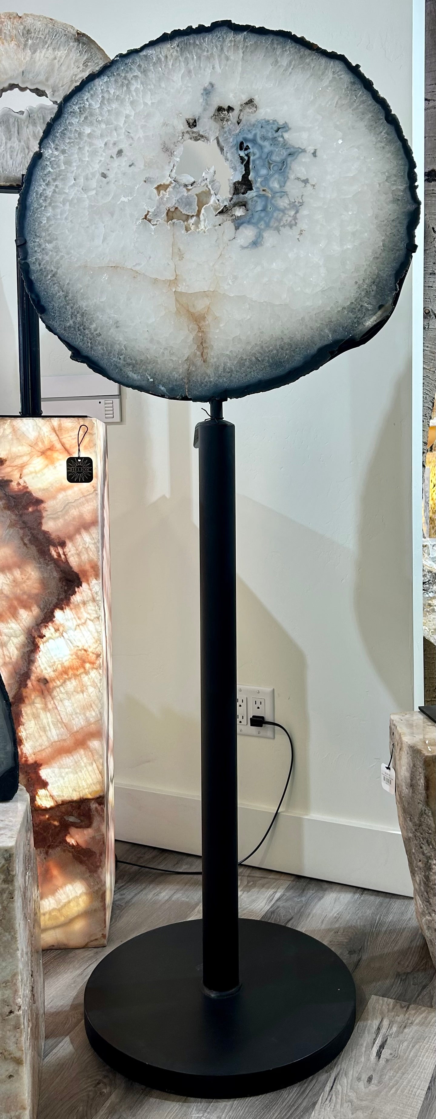 Introduce elegance to your space with our Lollipop Agate Revolving Slab. This unique piece features a stunning lollipop agate slab, securely mounted on a swivel stand for easy viewing. Sliced from a geode, this exquisite slab brings natural beauty and sophistication to any room.Measures approx. 27 1/4"W x 66"H (with stand). Lollipop Agate Revolving Slab