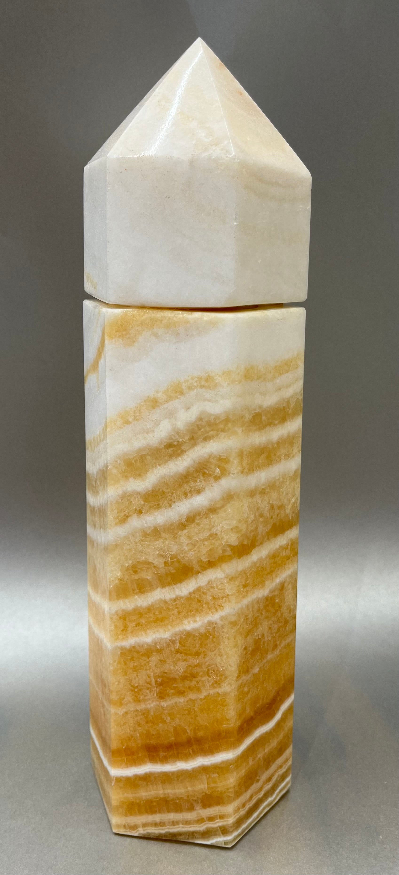 Indulge in the luxury of our Striped Calcite Obelisk Container. Crafted with a stunning striped calcite, this obelisk container doubles as a holder for your precious belongings or even more rock minerals! With its elegant silhouette, it adds a touch of sophistication to any space. Elevate your surroundings with this exclusive and timeless piece.Measures approx. 10.5" x 3". Striped Calcite Obelisk Container