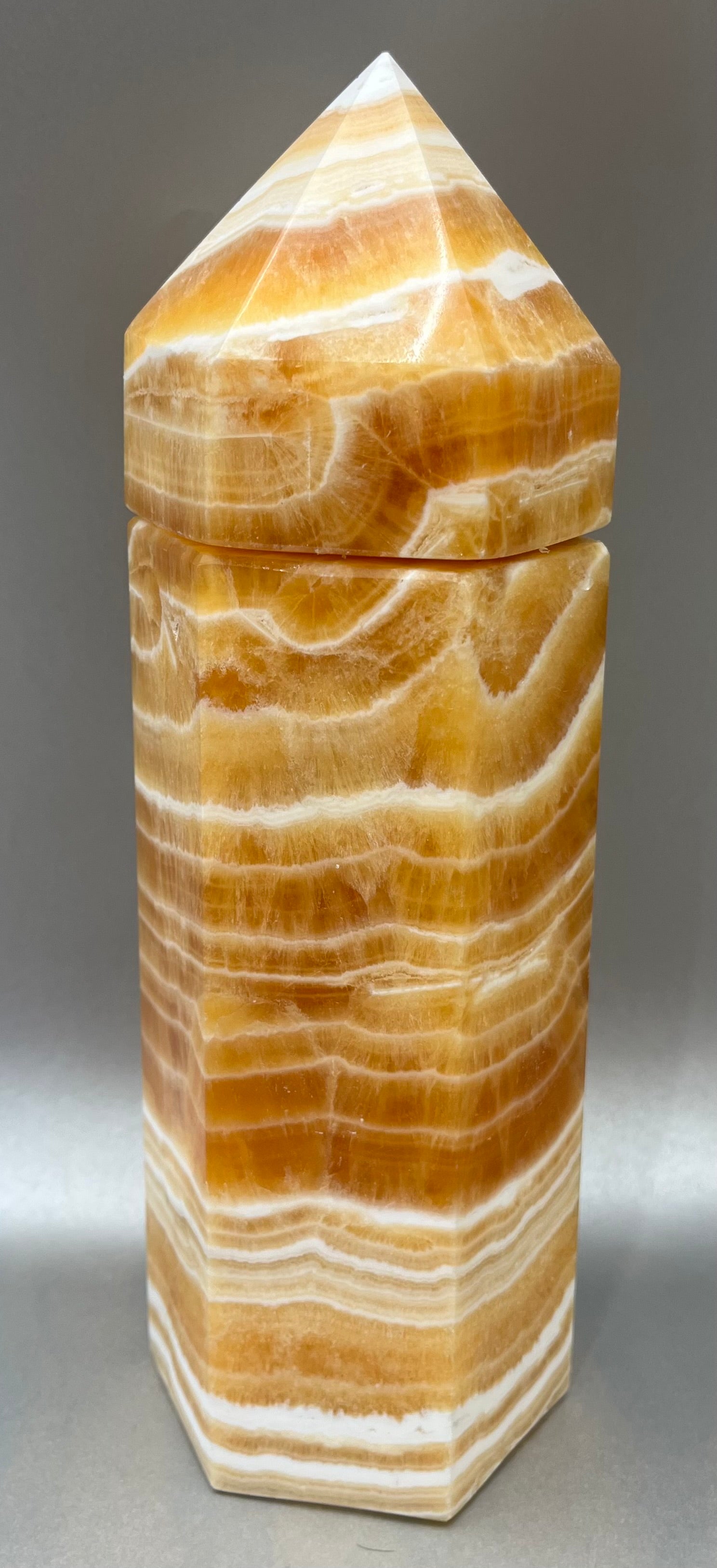Indulge in the luxury of our Striped Calcite Obelisk Container. Crafted with a stunning striped calcite, this obelisk container doubles as a holder for your precious belongings or even more rock minerals! With its elegant silhouette, it adds a touch of sophistication to any space. Elevate your surroundings with this exclusive and timeless piece.Measures approx. 9.5" x 3". Striped Calcite Obelisk Container