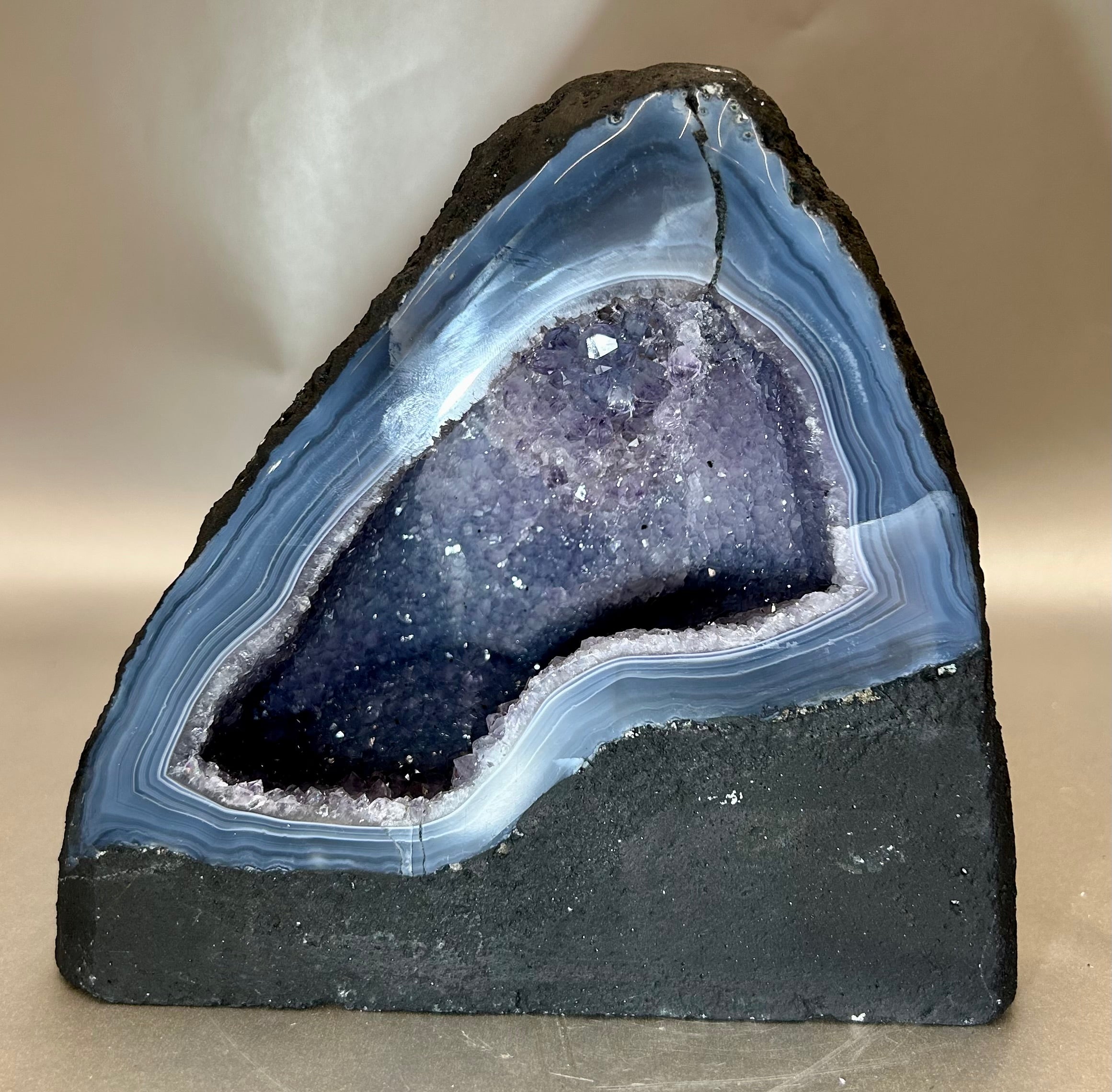 Embrace the enchanting beauty and mystical powers of our Amethyst Cathedral. Carved from a single geode, this luxurious masterpiece features a stunning display of deep purple amethyst crystals. Enhance your space with its calming energy and add a touch of elegance to your decor.Approx. 7" W x 3.75" D x 6.5" H Amethyst Cathedral