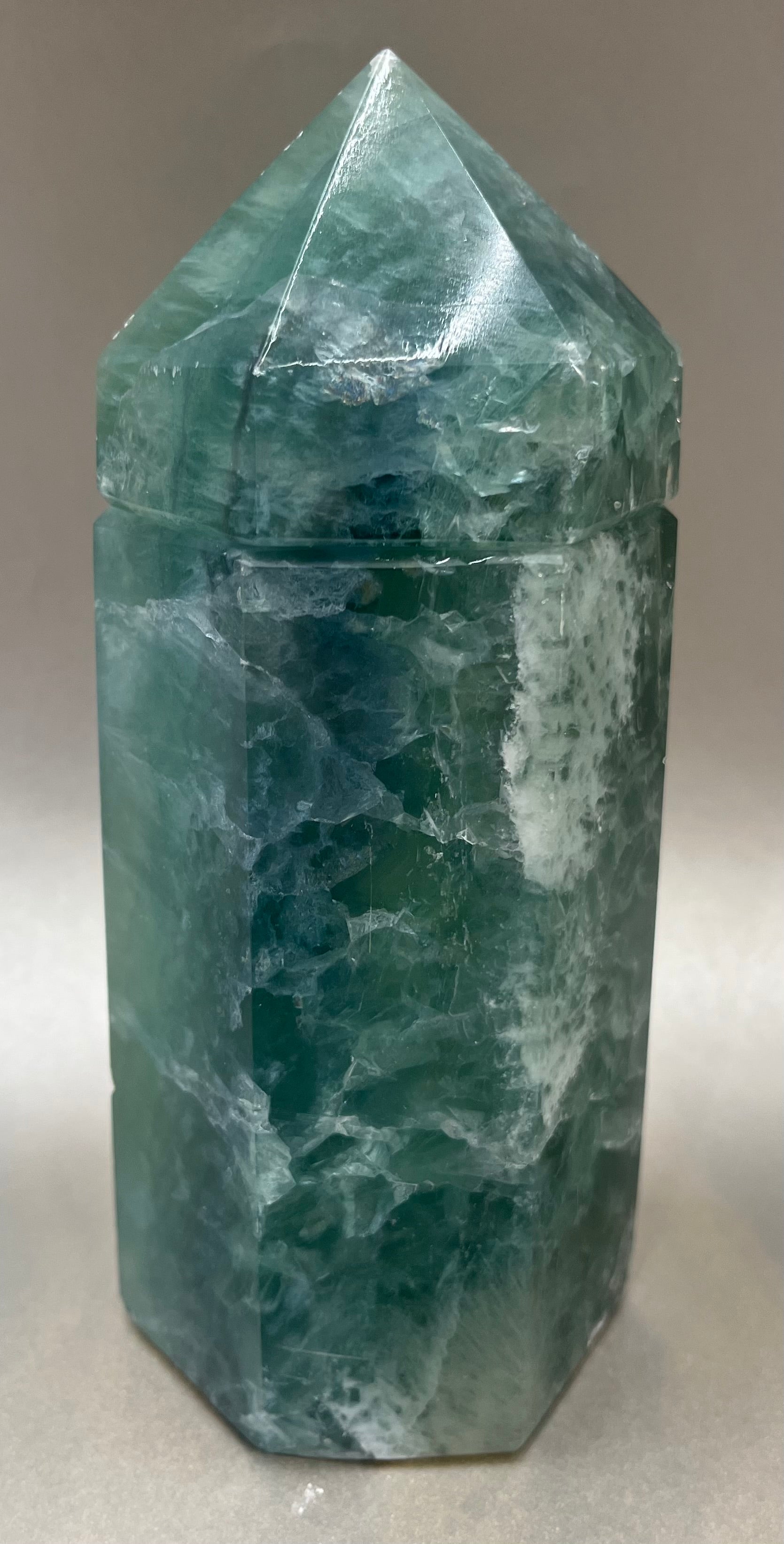 Indulge in the luxury of our Fluorite Obelisk Container. Crafted with a stunning fluorite, this obelisk container doubles as a holder for your precious belongings or even more rock minerals! With its elegant silhouette, it adds a touch of sophistication to any space. Elevate your surroundings with this exclusive and timeless piece.Measures approx. 6.5" x 2.5". Fluorite Obelisk Container