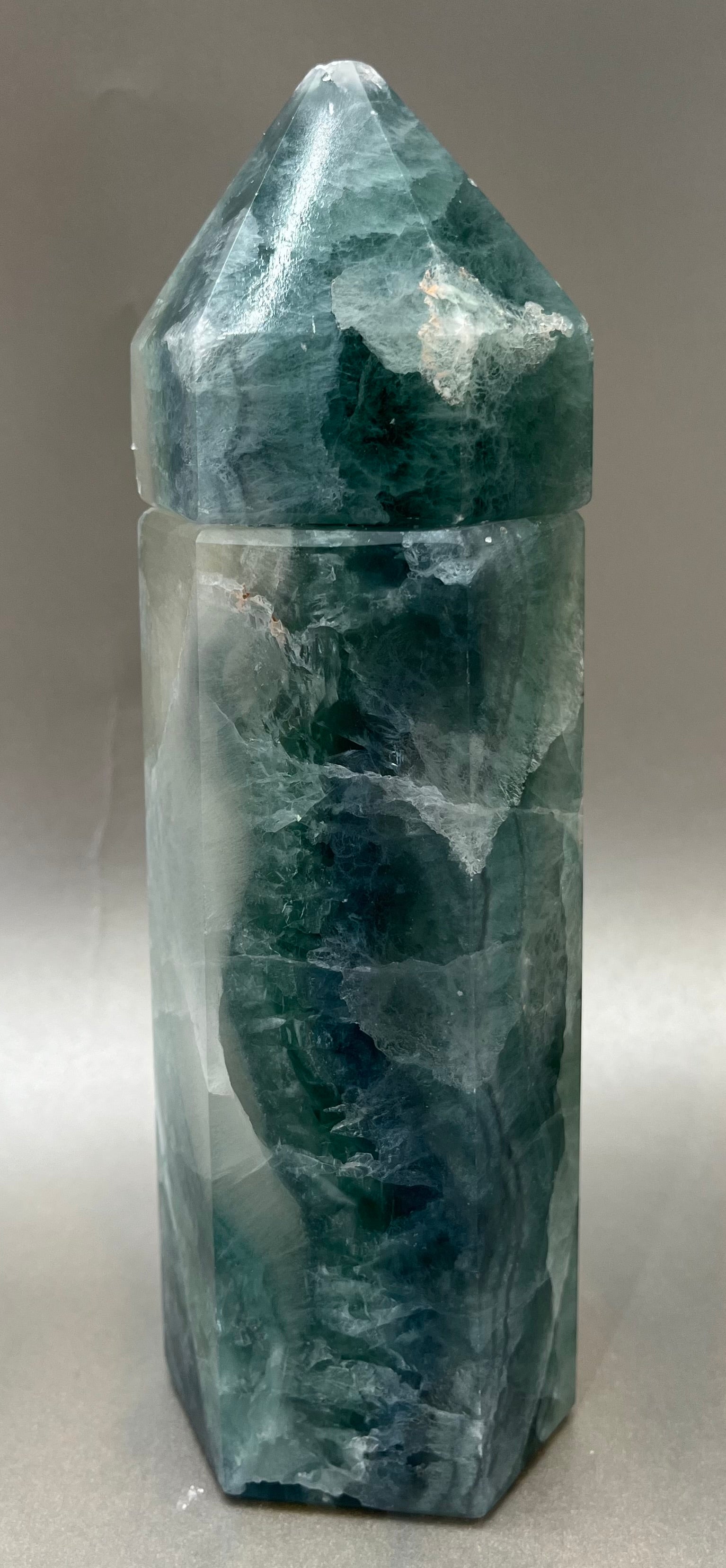 Indulge in the luxury of our Fluorite Obelisk Container. Crafted with a stunning fluorite, this obelisk container doubles as a holder for your precious belongings or even more rock minerals! With its elegant silhouette, it adds a touch of sophistication to any space. Elevate your surroundings with this exclusive and timeless piece.Measures approx. 8" x 2.5". Fluorite Obelisk Container
