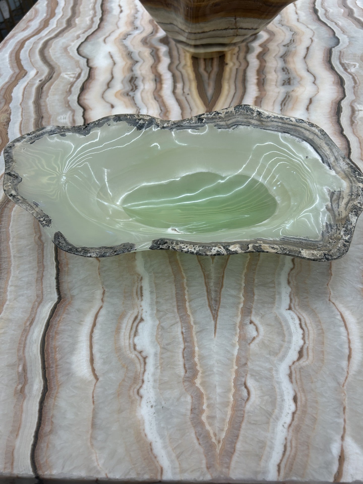 Indulge in the luxurious beauty of our Green Onyx Bowl. Hand carved from stunning green onyx, each bowl boasts a unique, freeform shape. Elevate your home decor with this exclusive piece, adding a touch of sophistication to any room. Experience the exquisite craftsmanship of this one-of-a-kind bowl.Approx. 15"L x 6.75"W x 4"H Green Onyx Bowl