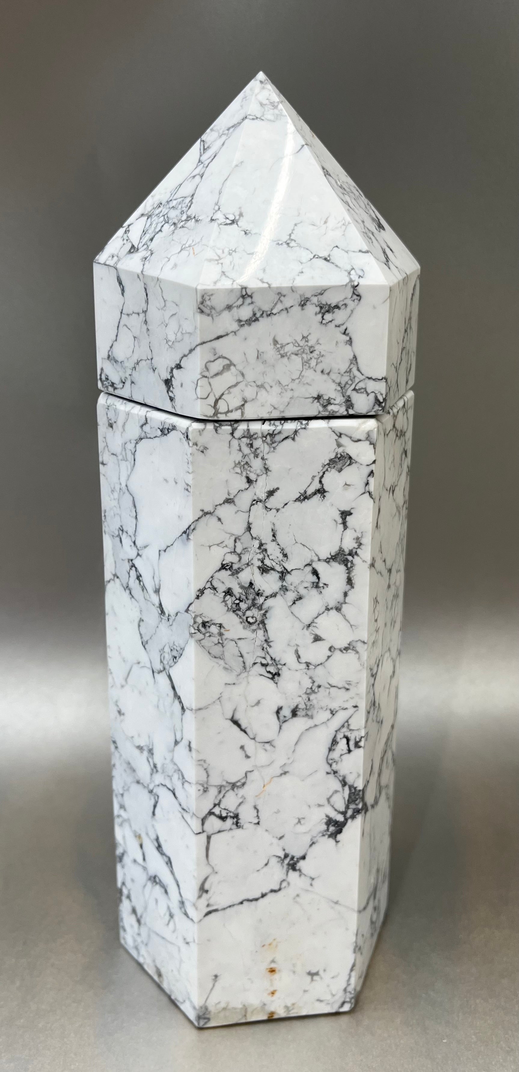 Indulge in the luxury of our White Howlite Obelisk Container. Crafted with a stunning white howlite, this obelisk container doubles as a holder for your precious belongings or even more rock minerals! With its elegant silhouette, it adds a touch of sophistication to any space. Elevate your surroundings with this exclusive and timeless piece.Measures approx. 9.5" x 3". White Howlite Obelisk Container