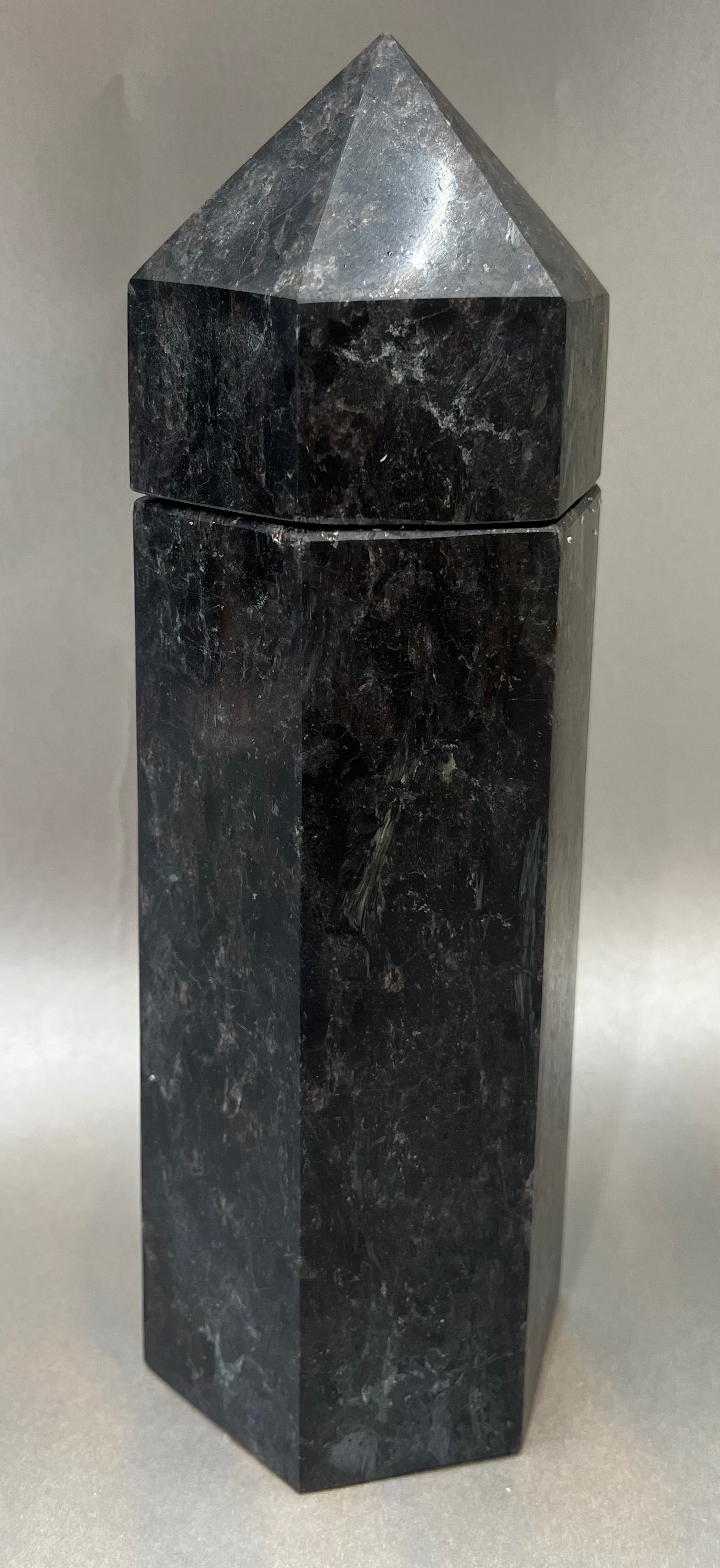 Indulge in the luxury of our Black Howlite Obelisk Container. Crafted with a stunning black howlite, this obelisk container doubles as a holder for your precious belongings or even more rock minerals! With its elegant silhouette, it adds a touch of sophistication to any space. Elevate your surroundings with this exclusive and timeless piece.Measures approx. 9" x 3". Black Howlite Obelisk Container