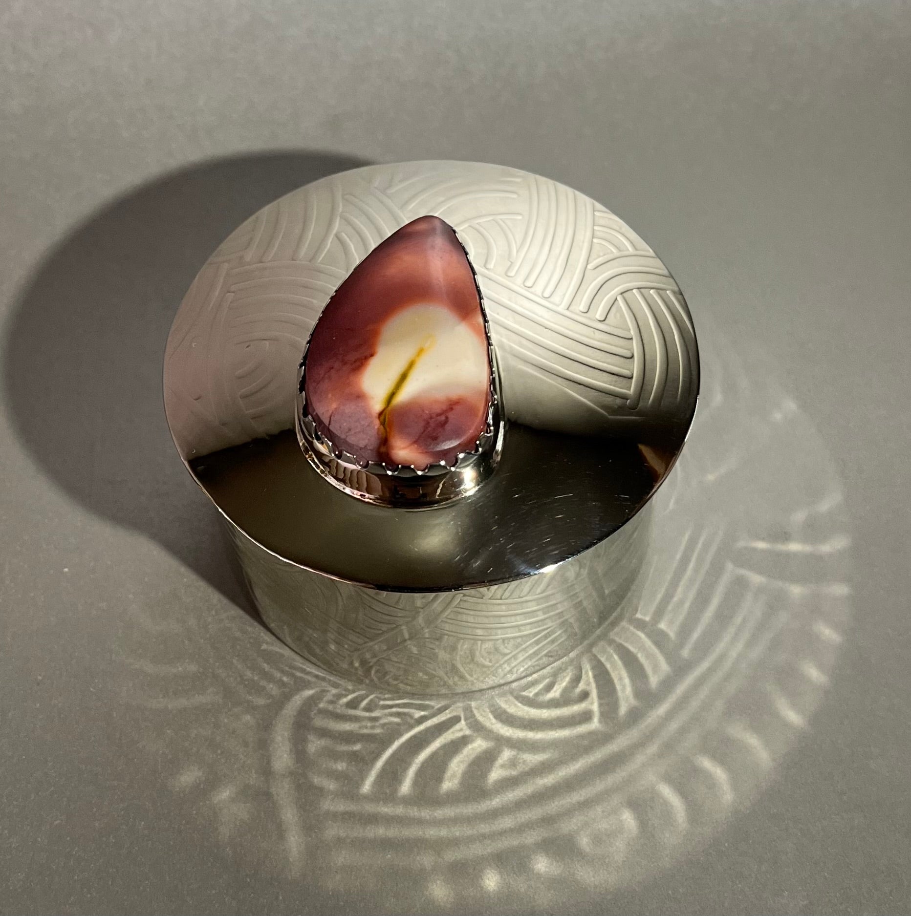 This nickel silver round treasure box features a hand-forged, silver-soldered, acid-etched design and is lined with leather, and includes a Mookaite Jasper piece. Approx. 2.5" diameter, 1.5" tall. Nickel Silver Round Treasure Box w/ Mookaite Jasper