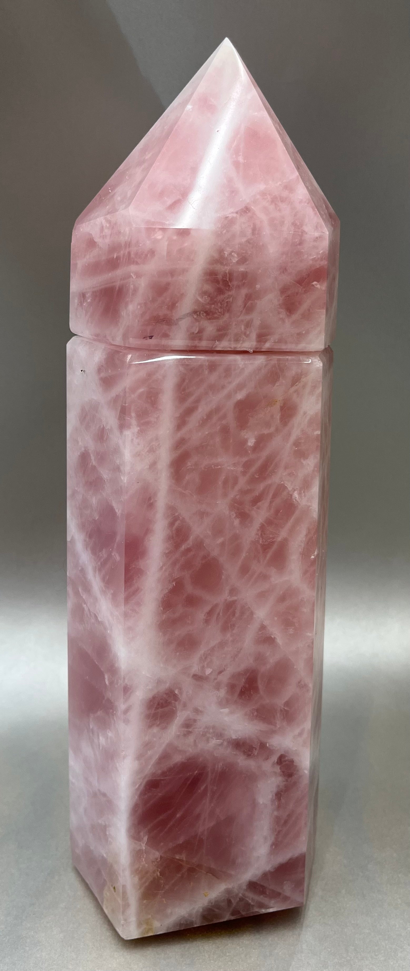 Indulge in the luxury of our Rose Quartz Obelisk Container. Crafted with a stunning rose quartz, this obelisk container doubles as a holder for your precious belongings or even more rock minerals! With its elegant silhouette, it adds a touch of sophistication to any space. Elevate your surroundings with this exclusive and timeless piece.Measures approx. 11.5" x 3.5". Rose Quartz Obelisk Container