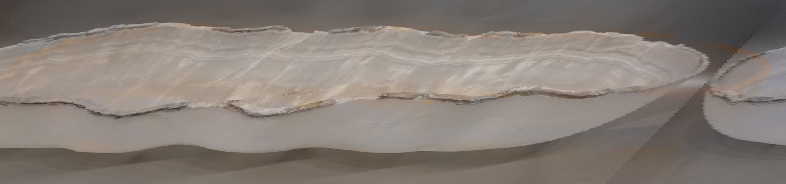 Indulge in the beauty of the Rustic Onyx Trough, handcrafted with natural rustic onyx displaying stunning veins. Its unique freeform shape adds a touch of sophistication to any space. Elevate your home with this luxurious piece, sure to impress and evoke admiration.Approx. 47" x 11" x 5" Rustic Onyx Trough