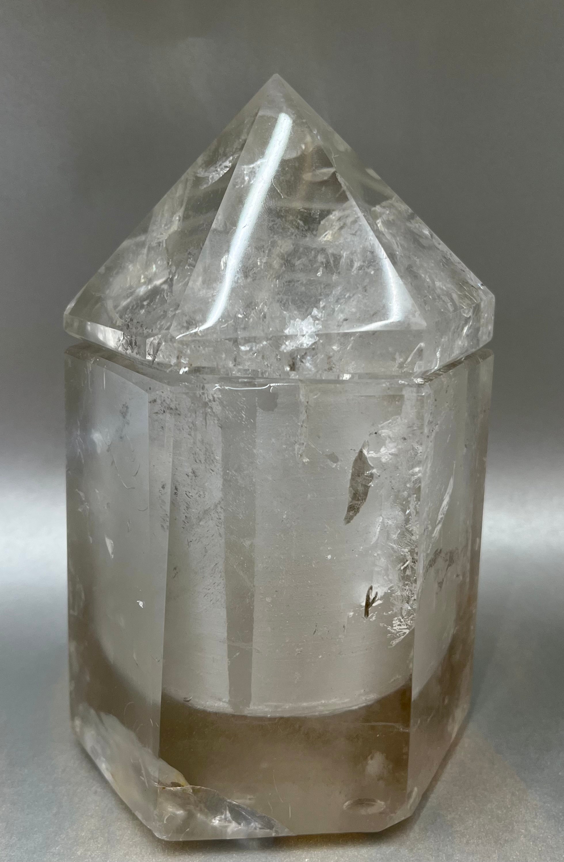 Indulge in the luxury of our Smokey Quartz Obelisk Container. Crafted with a stunning smokey quartz, this obelisk container doubles as a holder for your precious belongings or even more rock minerals! With its elegant silhouette, it adds a touch of sophistication to any space. Elevate your surroundings with this exclusive and timeless piece.Measures approx. 6.5" x 4". Quartz (Smokey) Obelisk Container