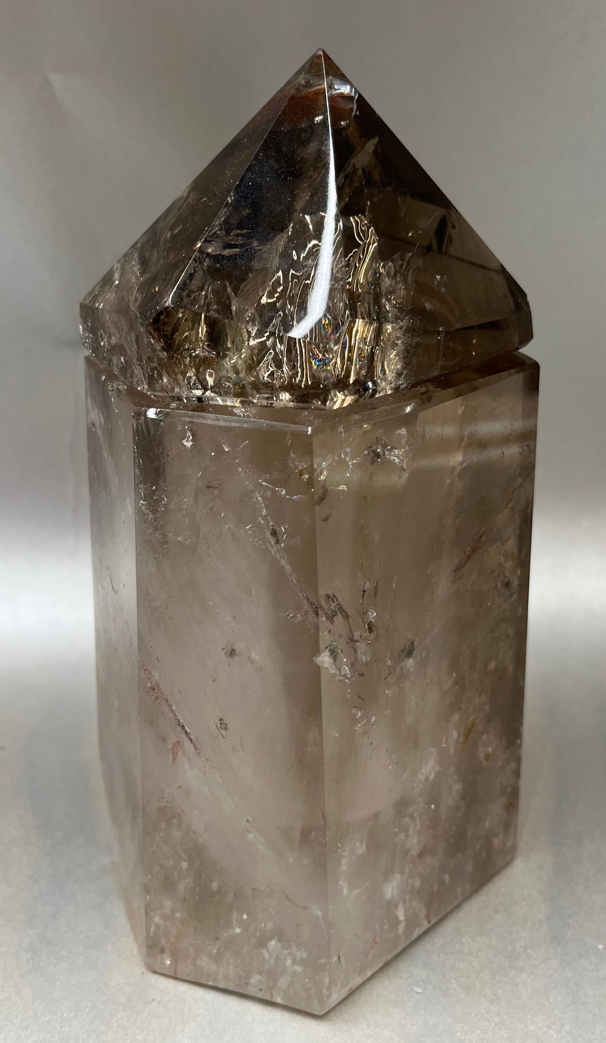 Indulge in the luxury of our Smokey Quartz Obelisk Container. Crafted with a stunning smokey quartz, this obelisk container doubles as a holder for your precious belongings or even more rock minerals! With its elegant silhouette, it adds a touch of sophistication to any space. Elevate your surroundings with this exclusive and timeless piece.Measures approx. 7" x 4". Quartz (Smokey) Obelisk Container