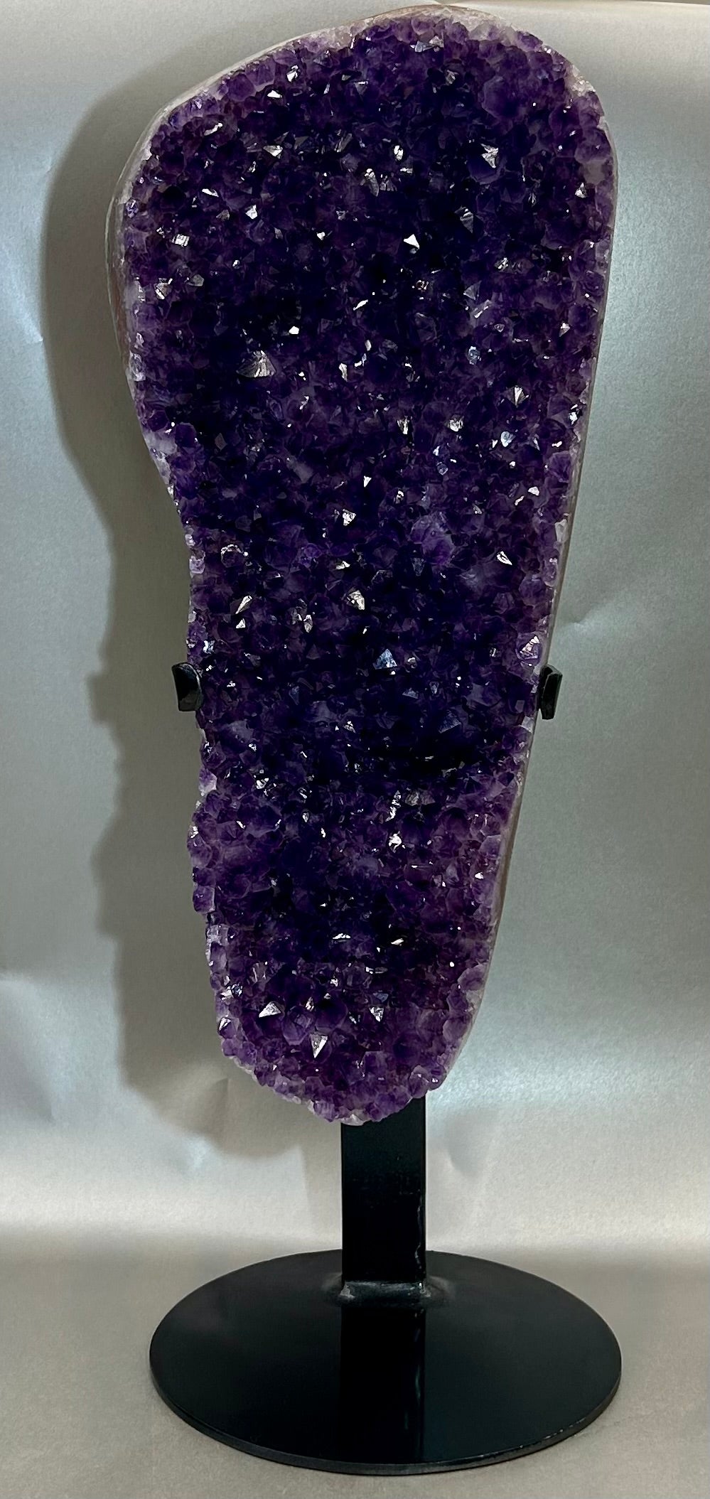 This amethyst on stand is the perfect addition to any home decor. Crafted with a premium natural amethyst crystal specimen and sturdy stand, this piece is sure to add a touch of elegance to any room. Its unparalleled beauty and durability make it a perfect long-term home accessory.The metal stand that comes with this piece is not permanently attached, it can be taken apart from the stand.Measured at 14.5" x 5" with stand. Uruguayan Amethyst on Stand