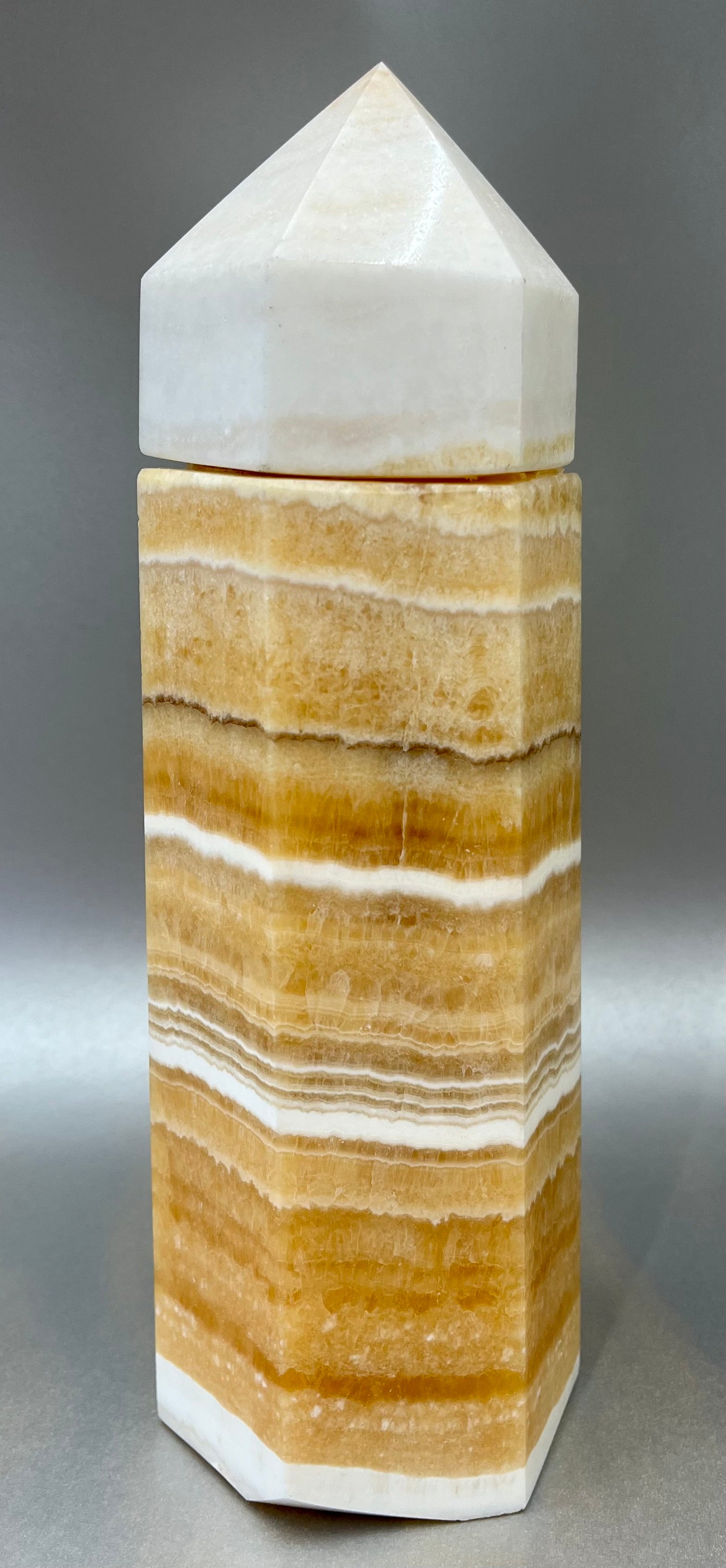 Indulge in the luxury of our Striped Calcite Obelisk Container. Crafted with a stunning striped calcite, this obelisk container doubles as a holder for your precious belongings or even more rock minerals! With its elegant silhouette, it adds a touch of sophistication to any space. Elevate your surroundings with this exclusive and timeless piece.Measures approx. 10" x 3". Striped Calcite Obelisk Container
