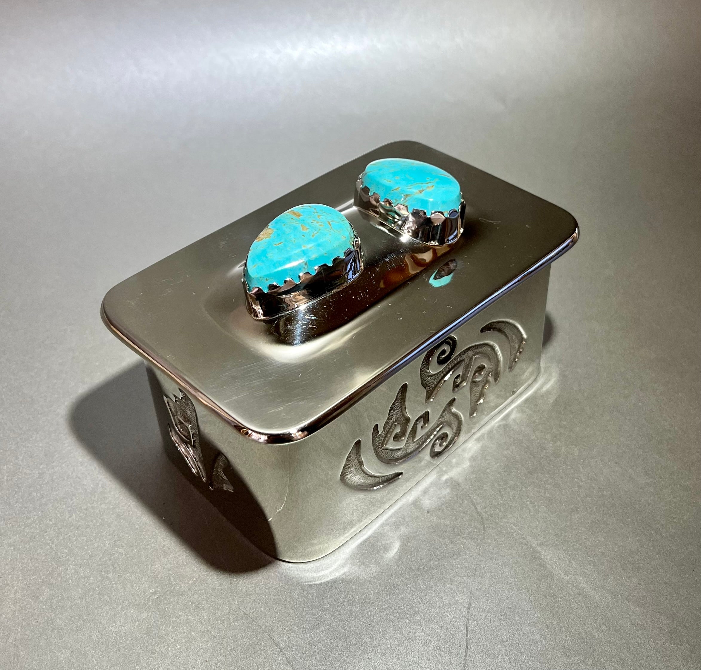 Crafted from nickel silver, this treasure box is accented with turquoise, meticulously hand forged and silver soldered, and delicately acid etched with a unique design. Lined with luxurious leather for a luxurious feel. 2.5" x 4". Nickel Silver Treasure Box w/ Turquoise