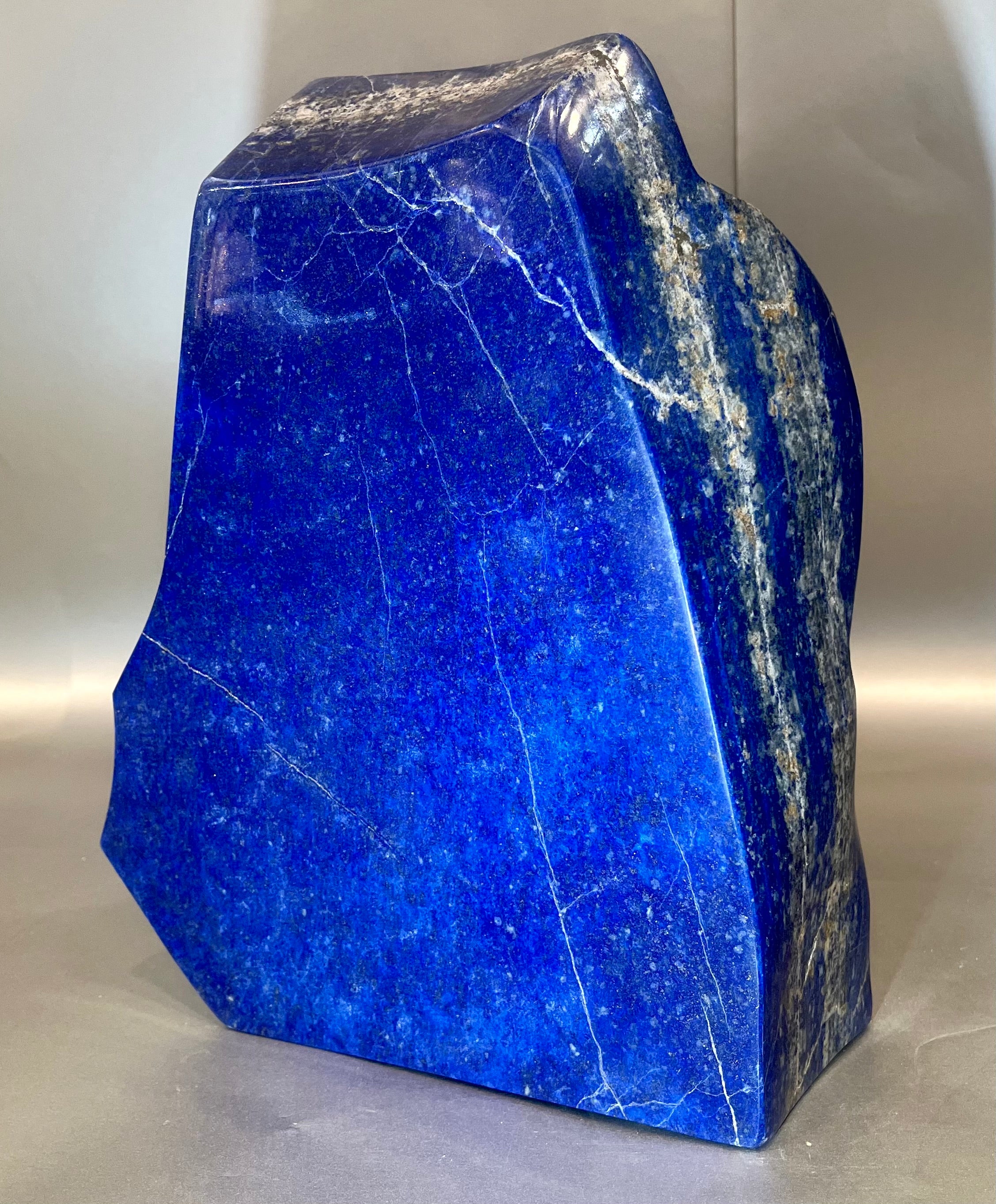 This large Lapis Lazuli specimen is a stunning gemstone known for its deep blue color, often with flecks of golden Pyrite scattered throughout. It has been used for centuries in jewelry and decor due to its captivating beauty. Lapis Lazuli is composed mainly of the mineral Lazurite, which gives it its vibrant blue hue. It's also believed to have metaphysical properties, such as promoting inner peace and enhancing wisdom. This large Lapis Lazuli specimen would certainly make a striking centerpiece in any collection or display. Approx. 11" x 8". Lapis Lazuli