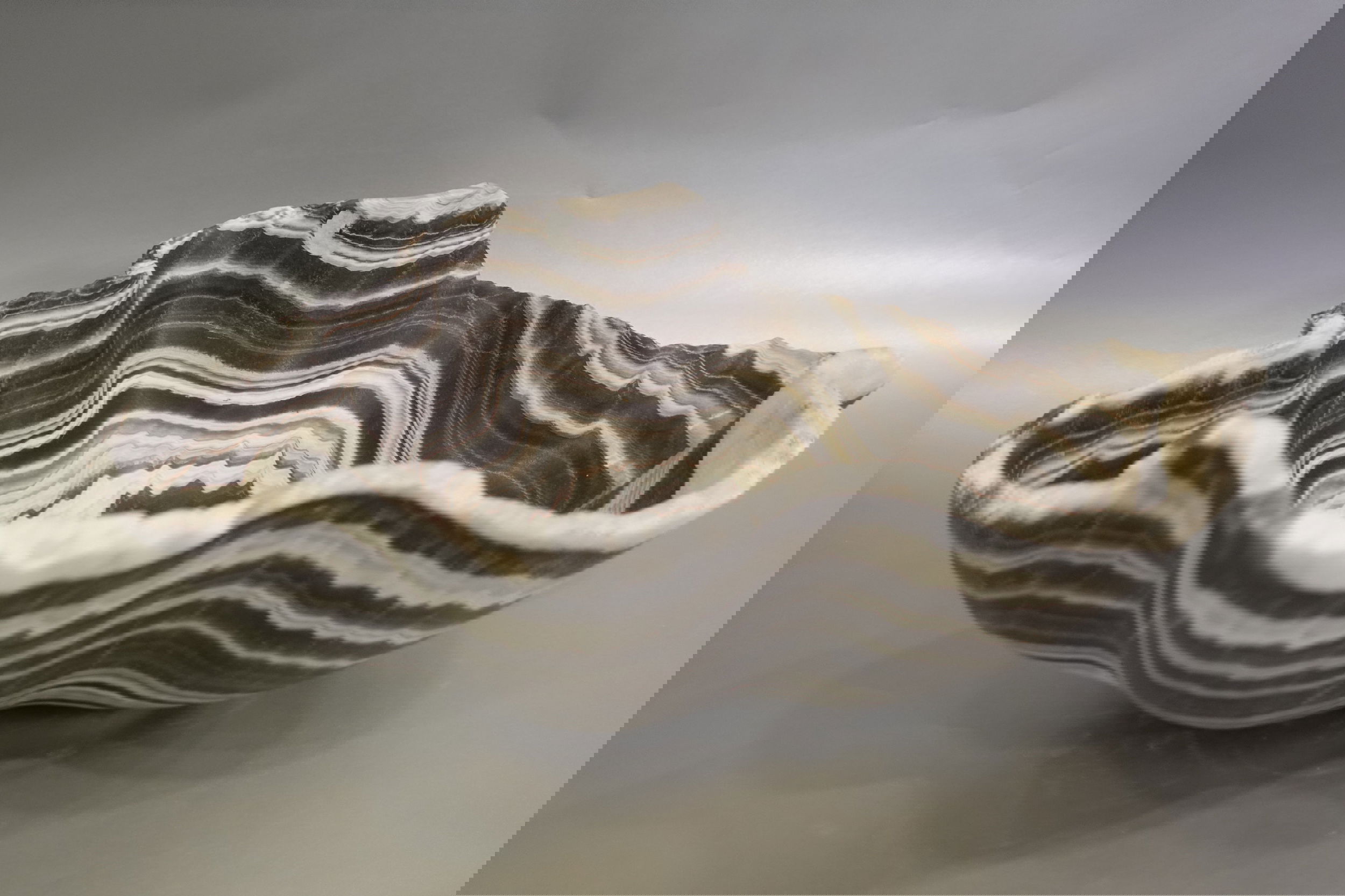 Indulge in the luxurious uniqueness of our Zebra Onyx Bowl. Its banded surface showcases the exquisite patterns of zebra onyx, while its distinct shape adds a touch of sophistication. Elevate your home decor with this exclusive piece that exudes elegance and refinement.Approx. 14.25" x 5" Zebra Onyx Bowl