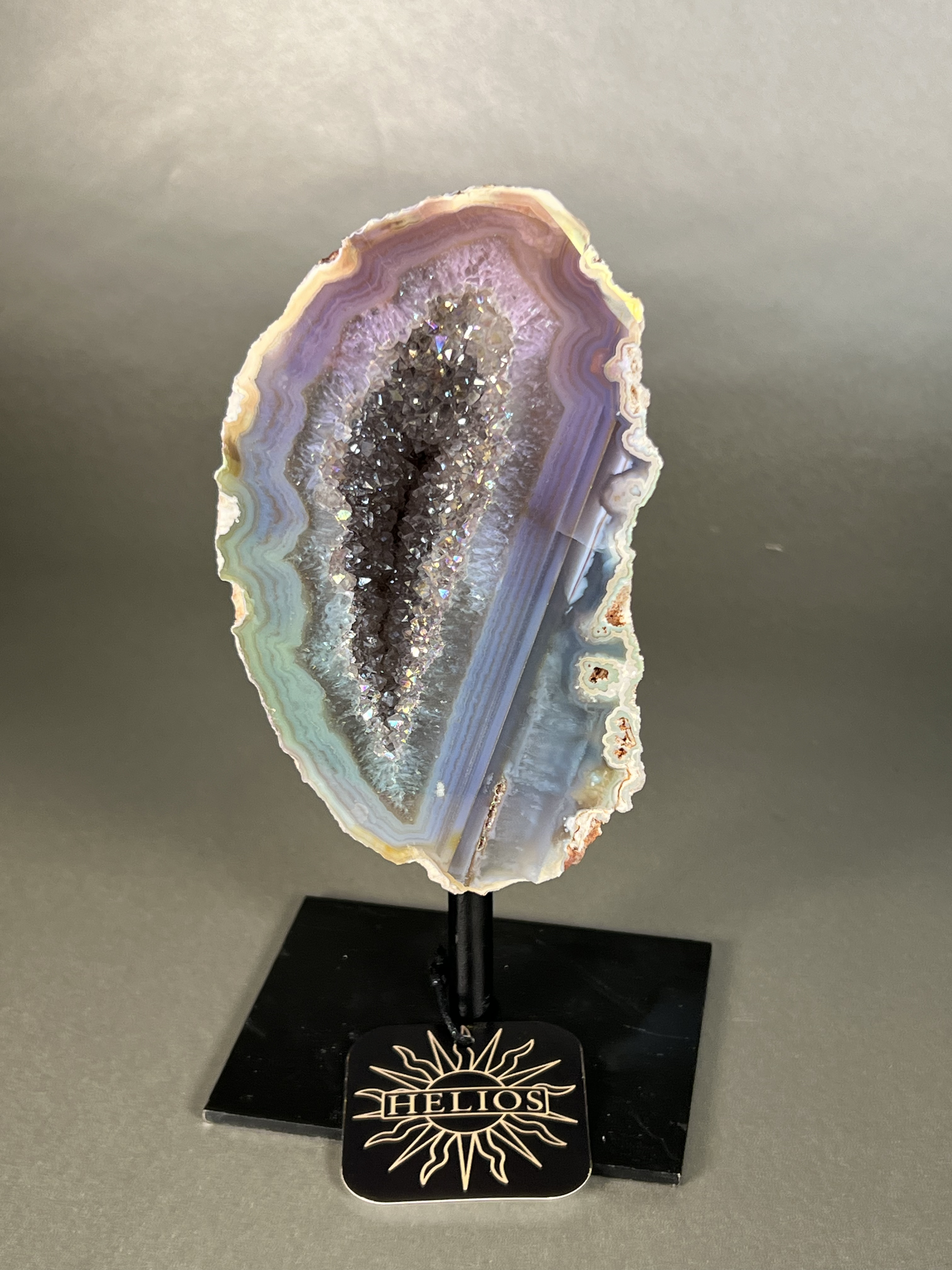 Experience the dreamy elegance of our Aura Agate Obelisk. Each one is uniquely crafted to exude a sense of luxury and exclusivity. Featuring the rare Aura Agate stone, this obelisk brings a touch of sophistication and beauty to any space. Elevate your decor with this truly one-of-a-kind piece. Approx. 4"x7.5" Aura Agate Geodes On Stand