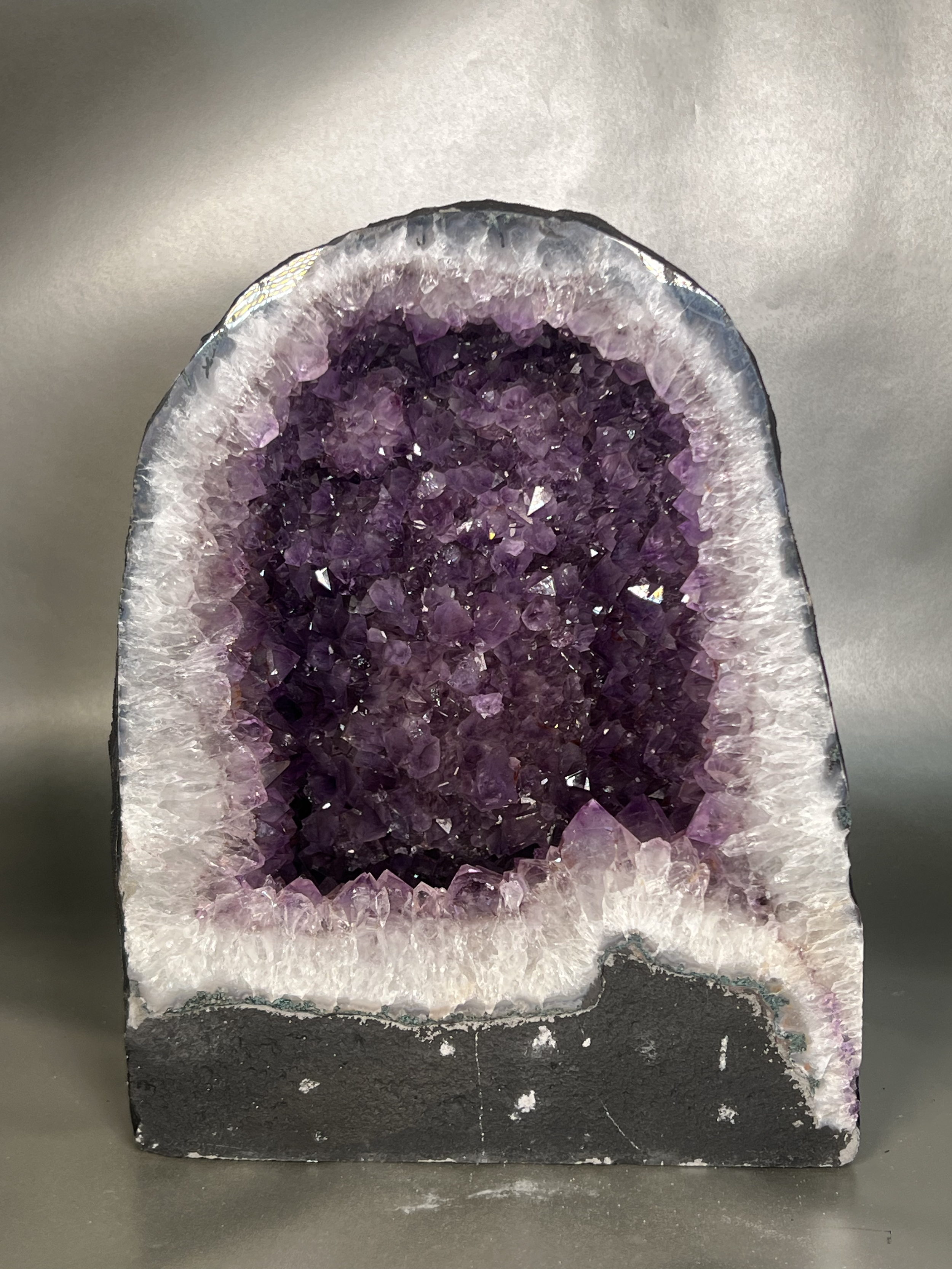 Embrace the enchanting beauty and mystical powers of our Amethyst Cathedral. Carved from a single geode, this luxurious masterpiece features a stunning display of deep purple amethyst crystals. Enhance your space with its calming energy and add a touch of elegance to your decor. Approx. 10" x 13" Amethyst Cathedral
