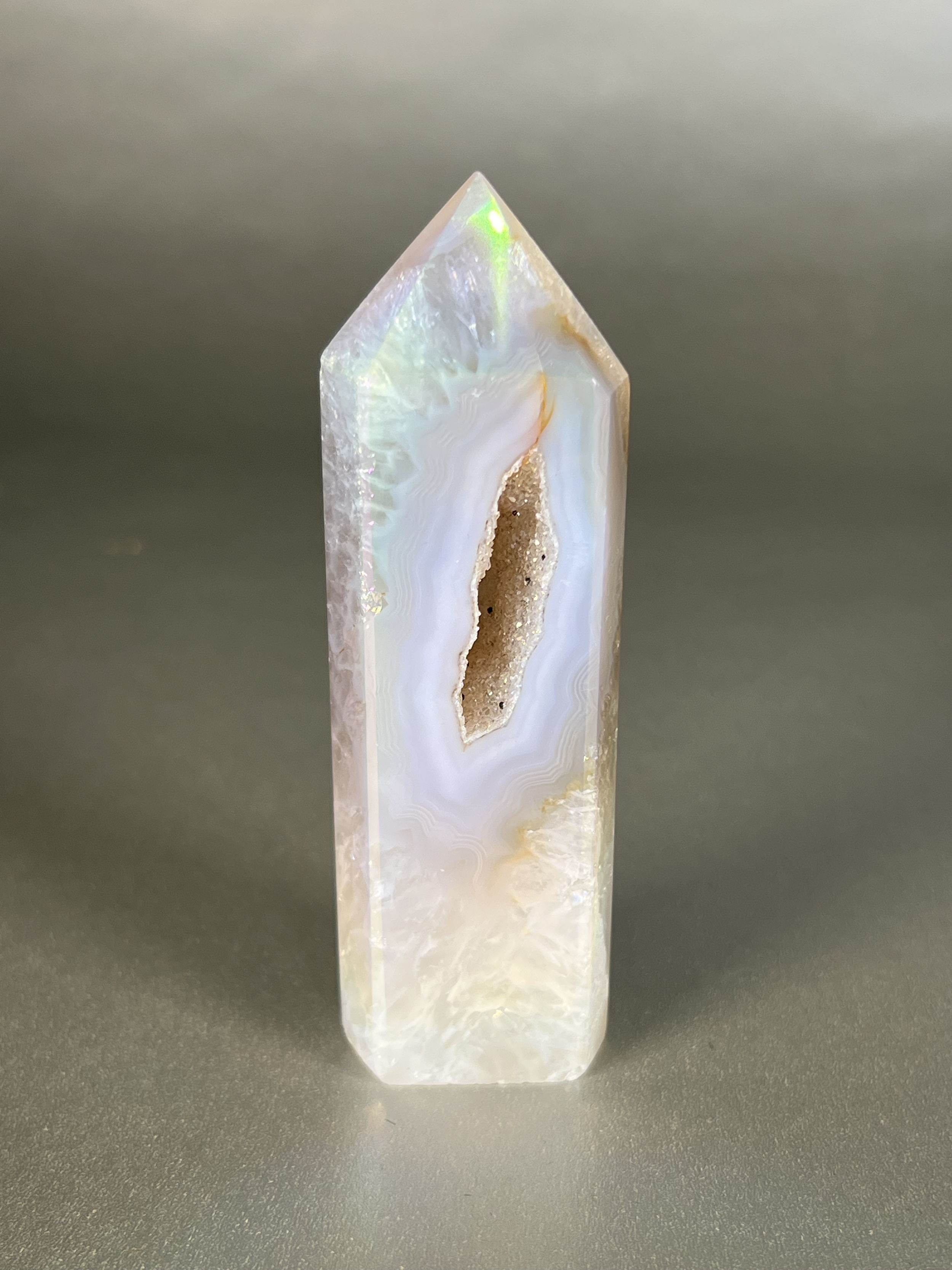 Experience the dreamy elegance of our Aura Agate Obelisk. Each one is uniquely crafted to exude a sense of luxury and exclusivity. Featuring the rare Aura Agate stone, this obelisk brings a touch of sophistication and beauty to any space. Elevate your decor with this truly one-of-a-kind piece. Approx. 1 "x 4" Aura Agate Tower