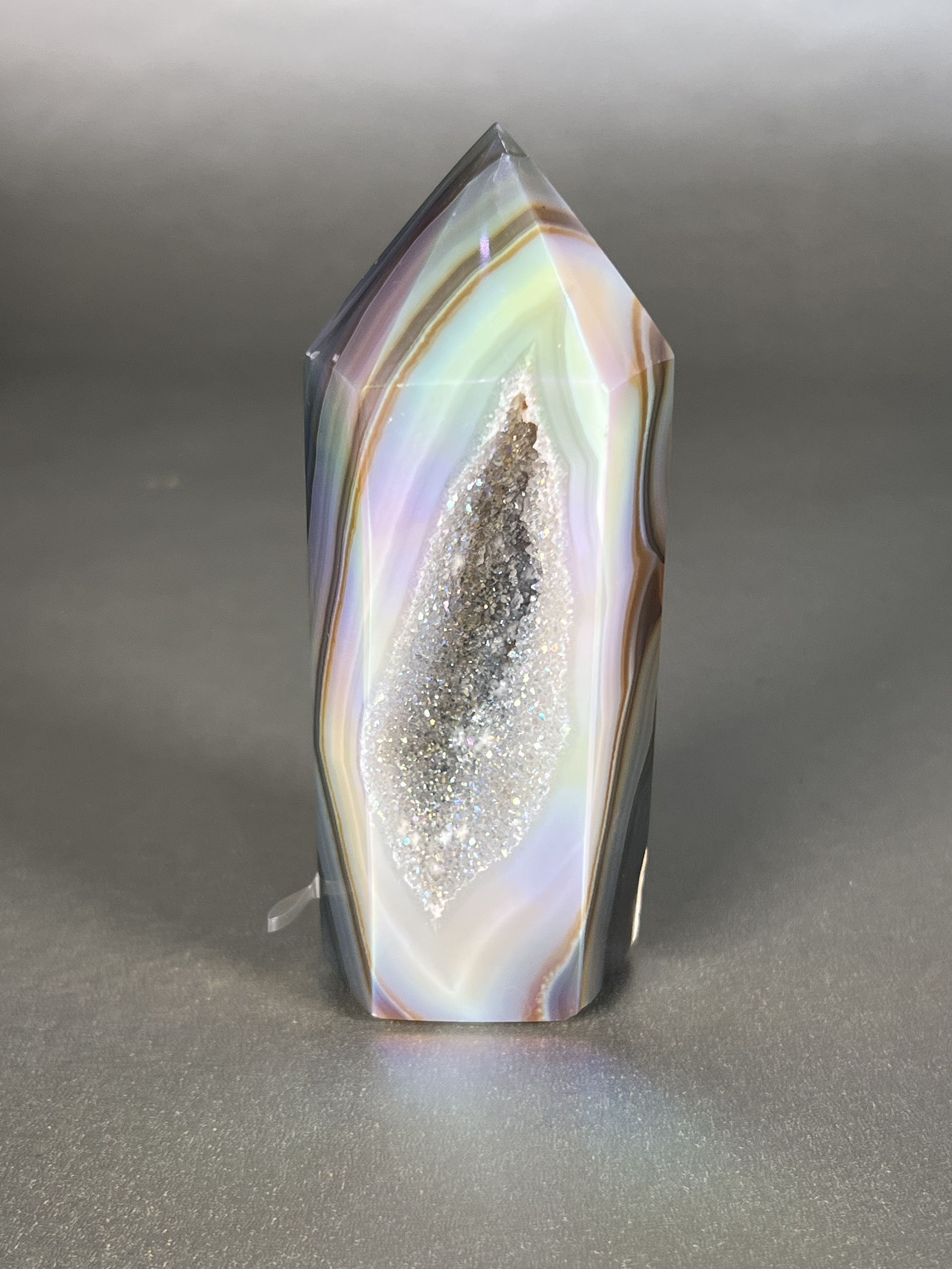 Experience the dreamy elegance of our Aura Agate Obelisk. Each one is uniquely crafted to exude a sense of luxury and exclusivity. Featuring the rare Aura Agate stone, this obelisk brings a touch of sophistication and beauty to any space. Elevate your decor with this truly one-of-a-kind piece. Approx. 1.5" x 4.5" Aura Agate Tower