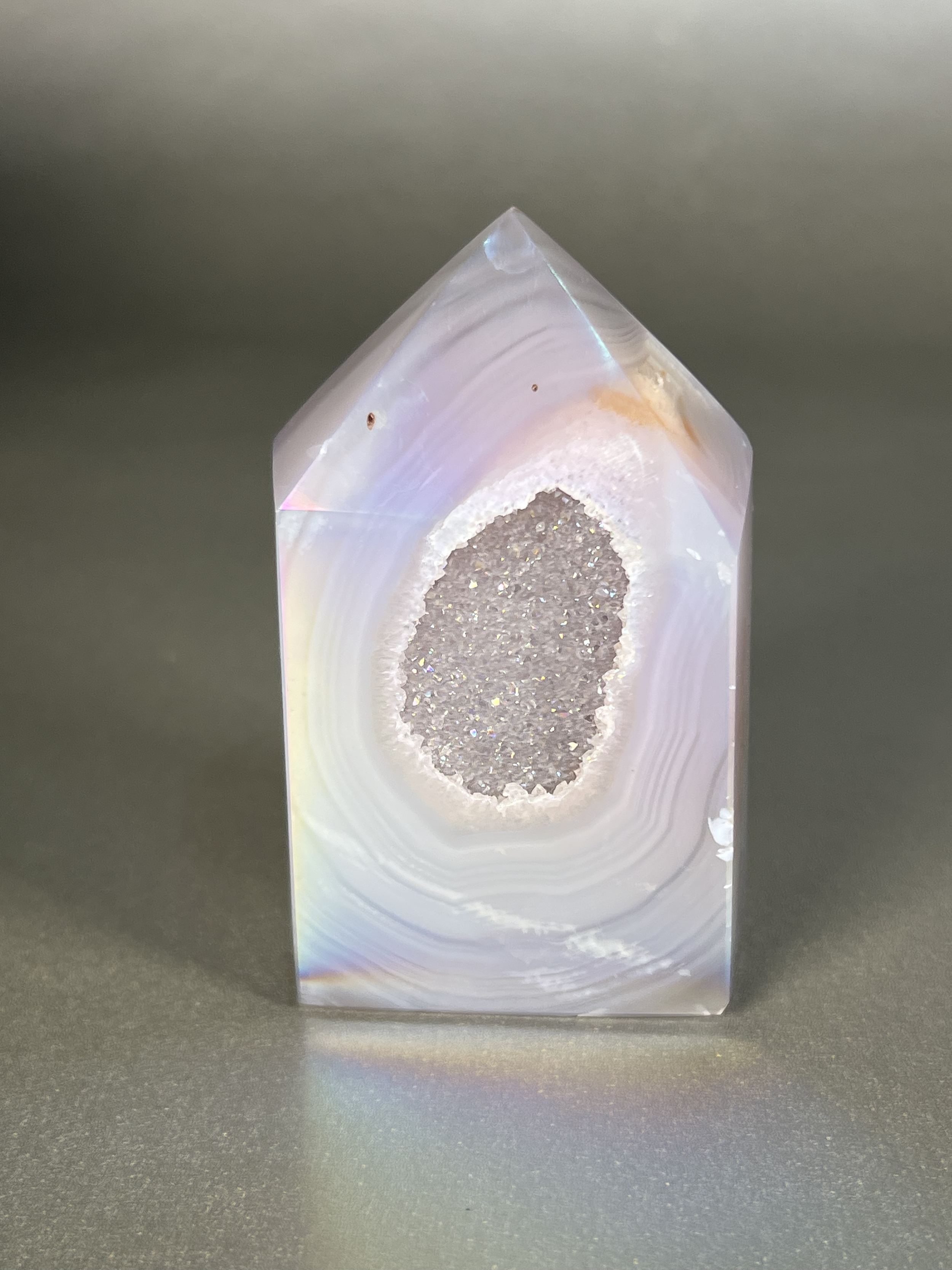 Experience the dreamy elegance of our Aura Agate Obelisk. Each one is uniquely crafted to exude a sense of luxury and exclusivity. Featuring the rare Aura Agate stone, this obelisk brings a touch of sophistication and beauty to any space. Elevate your decor with this truly one-of-a-kind piece. Approx. 2" x 3.5" Aura Agate Tower